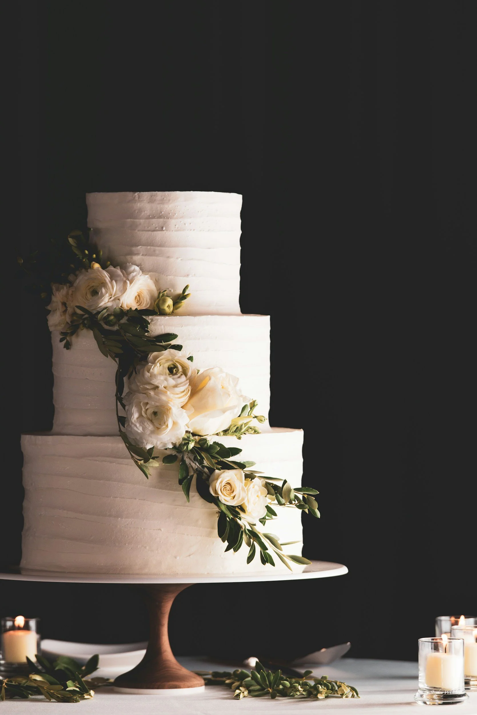 Elegant three-tier white wedding cake decorated with white roses and greenery.