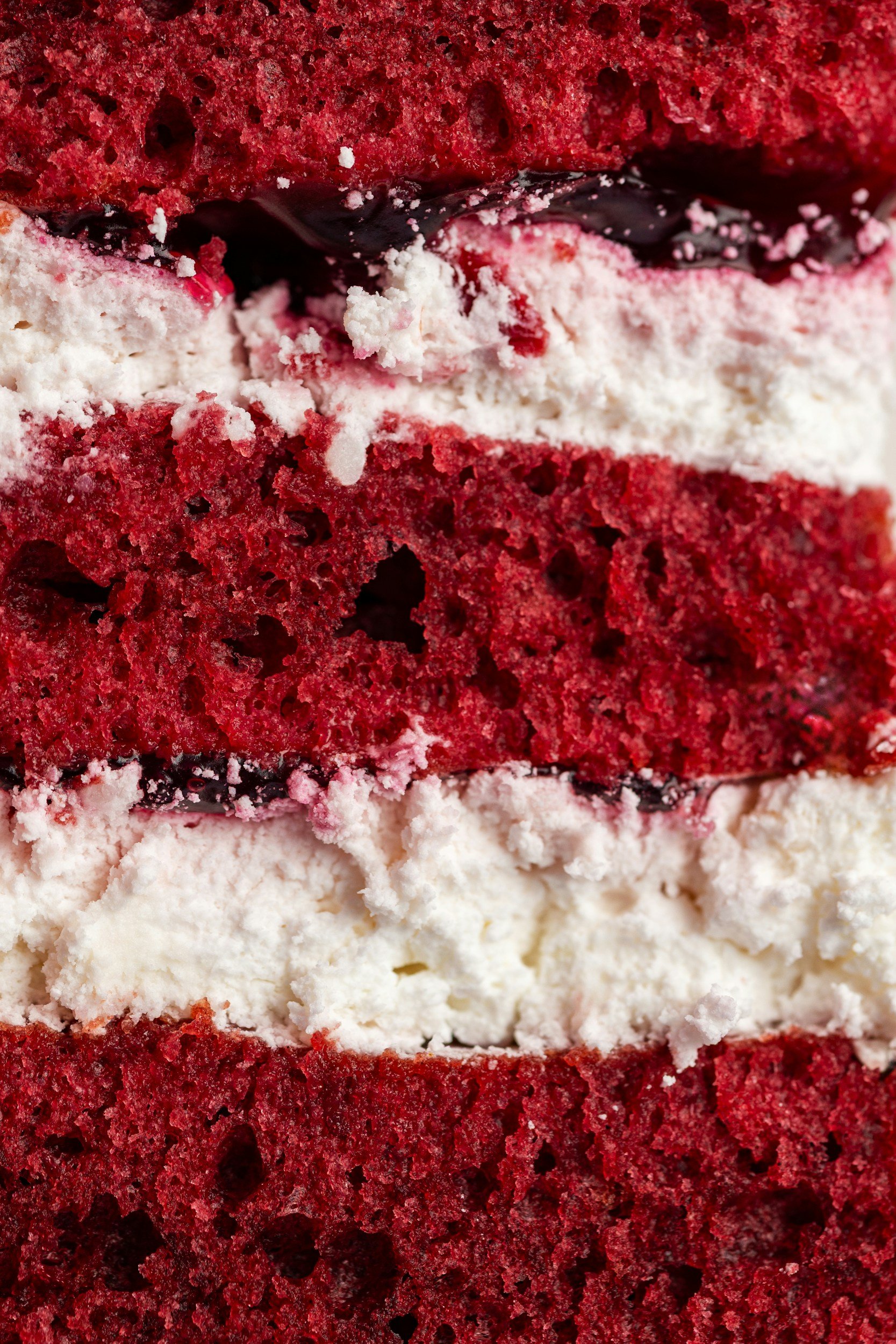 Close-up of layered red velvet cake with white frosting and berry filling.