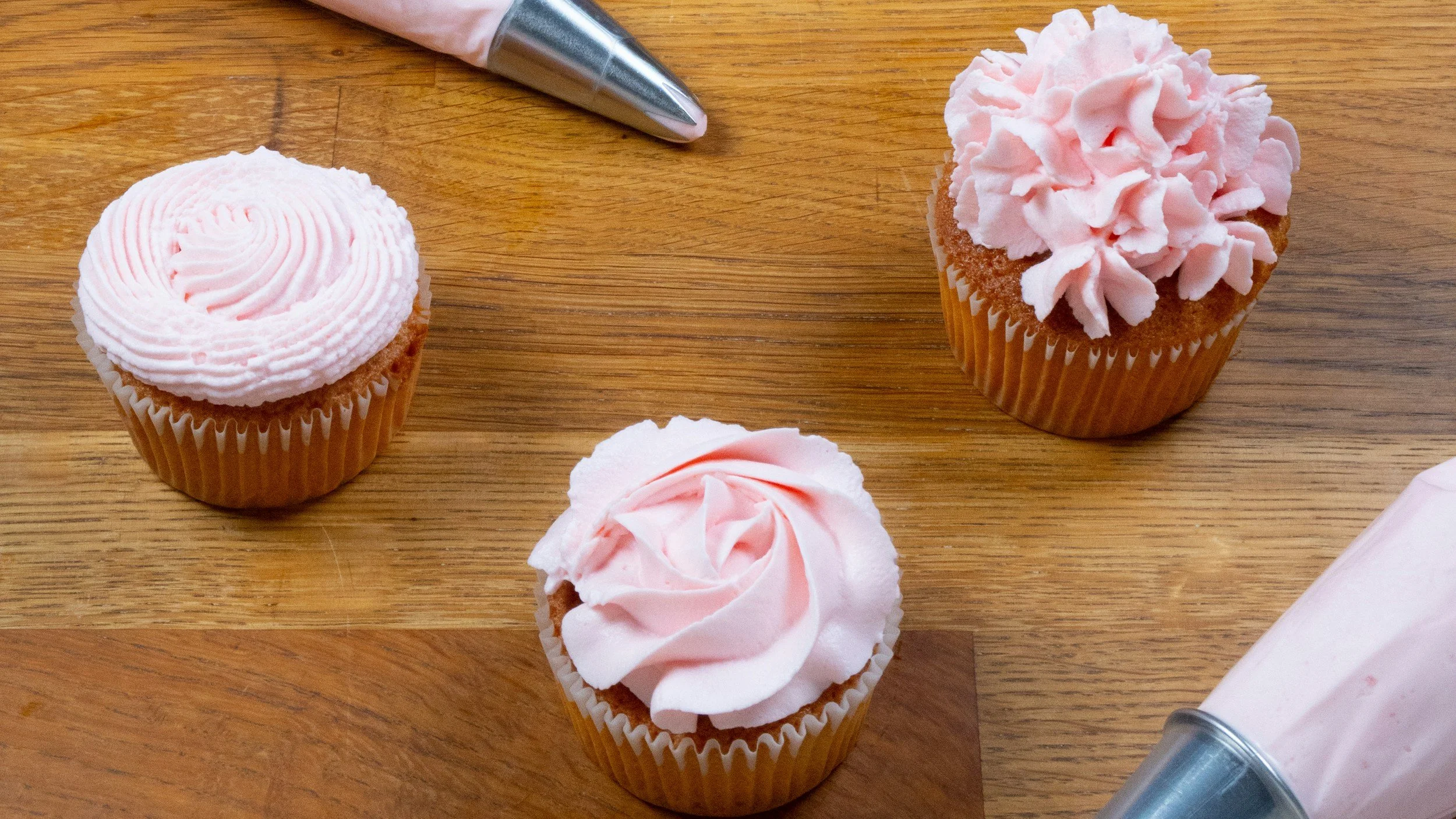 Three cupcakes decorated with pink piped buttercream swirls and rosettes.