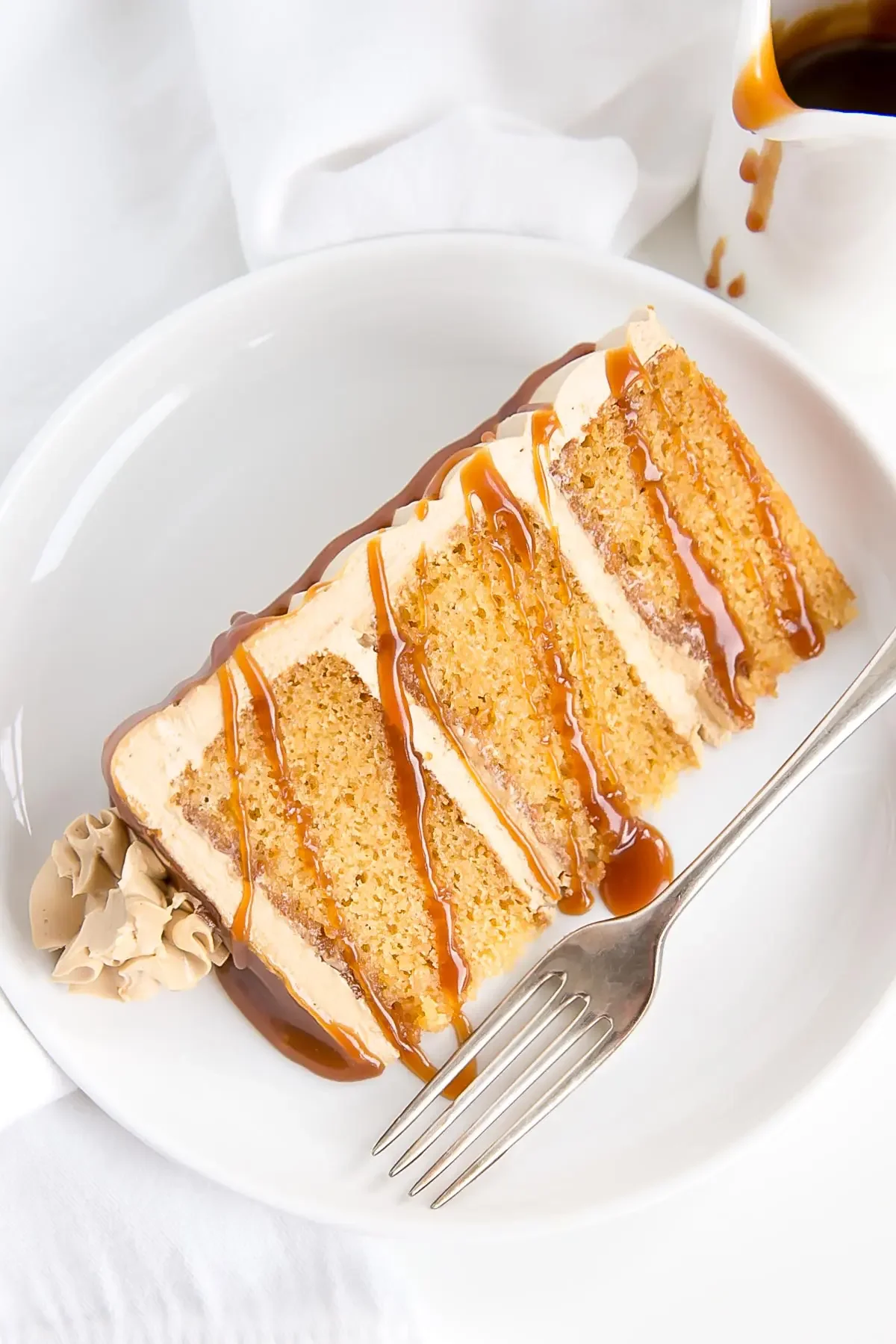 A slice of caramel cake topped with caramel drizzle, and buttercream frosting.