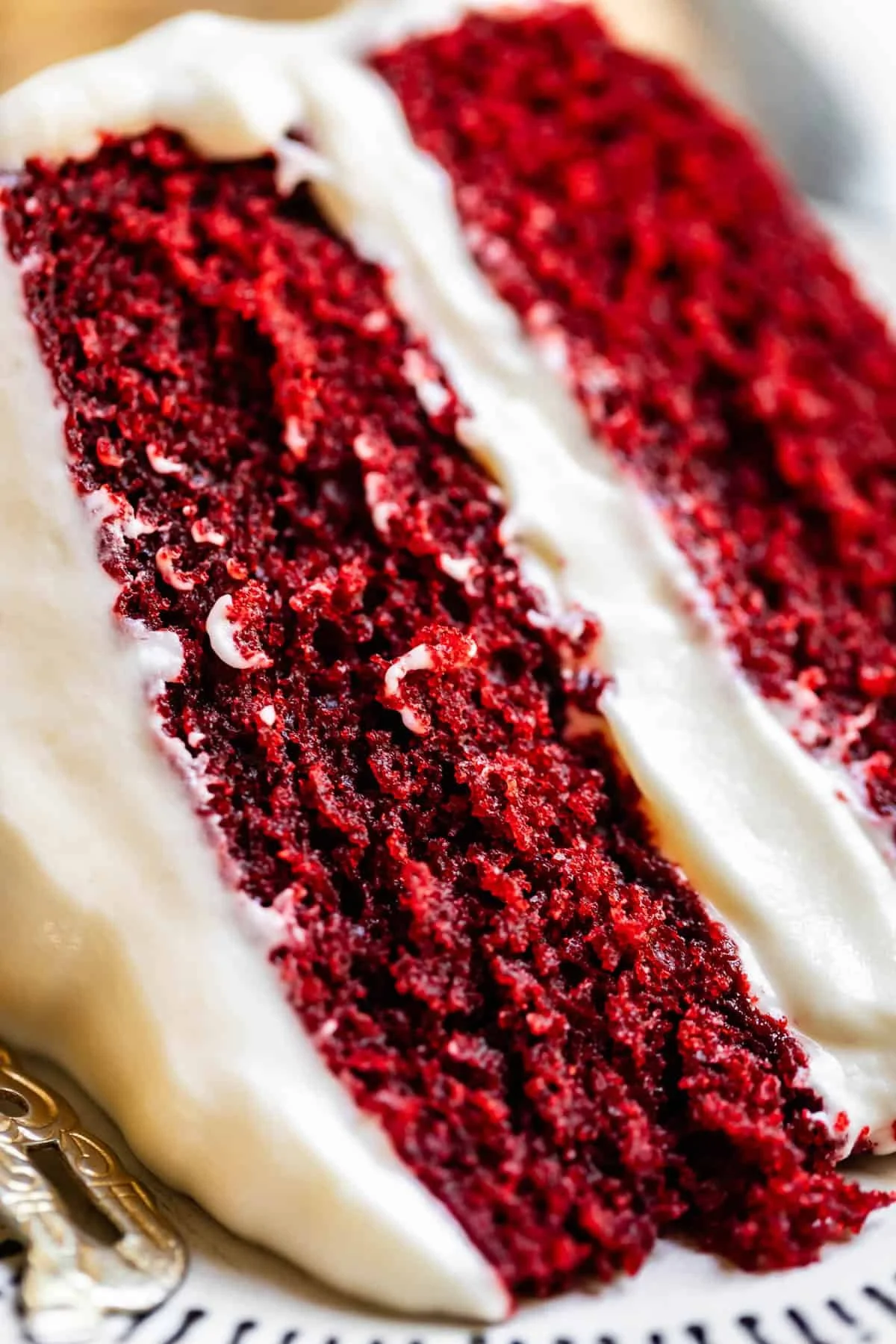 Close-up of a slice of red velvet cake with buttercream frosting on a decorative plate.