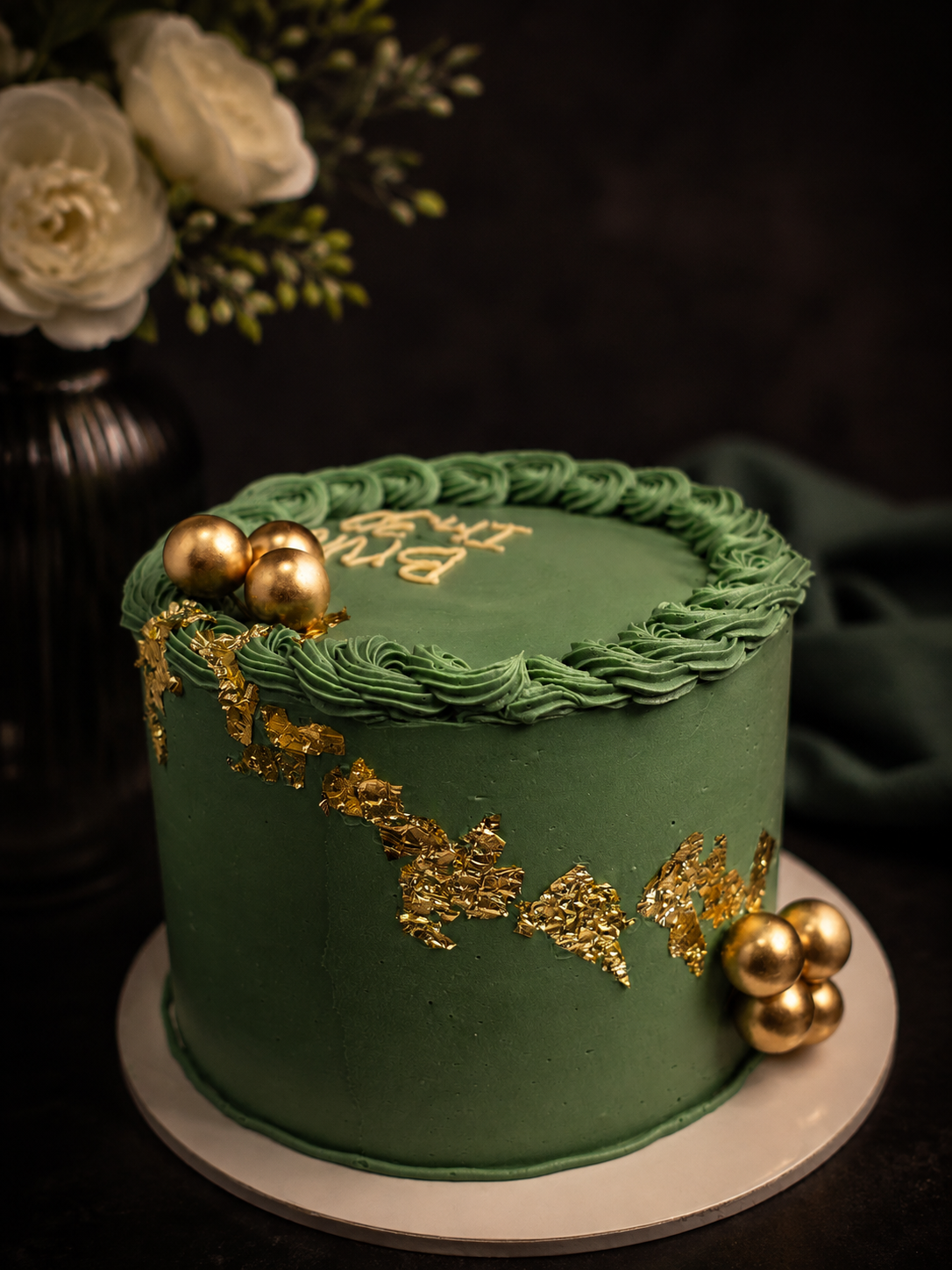 Green celebration cake decorated with gold accents and gold spheres.