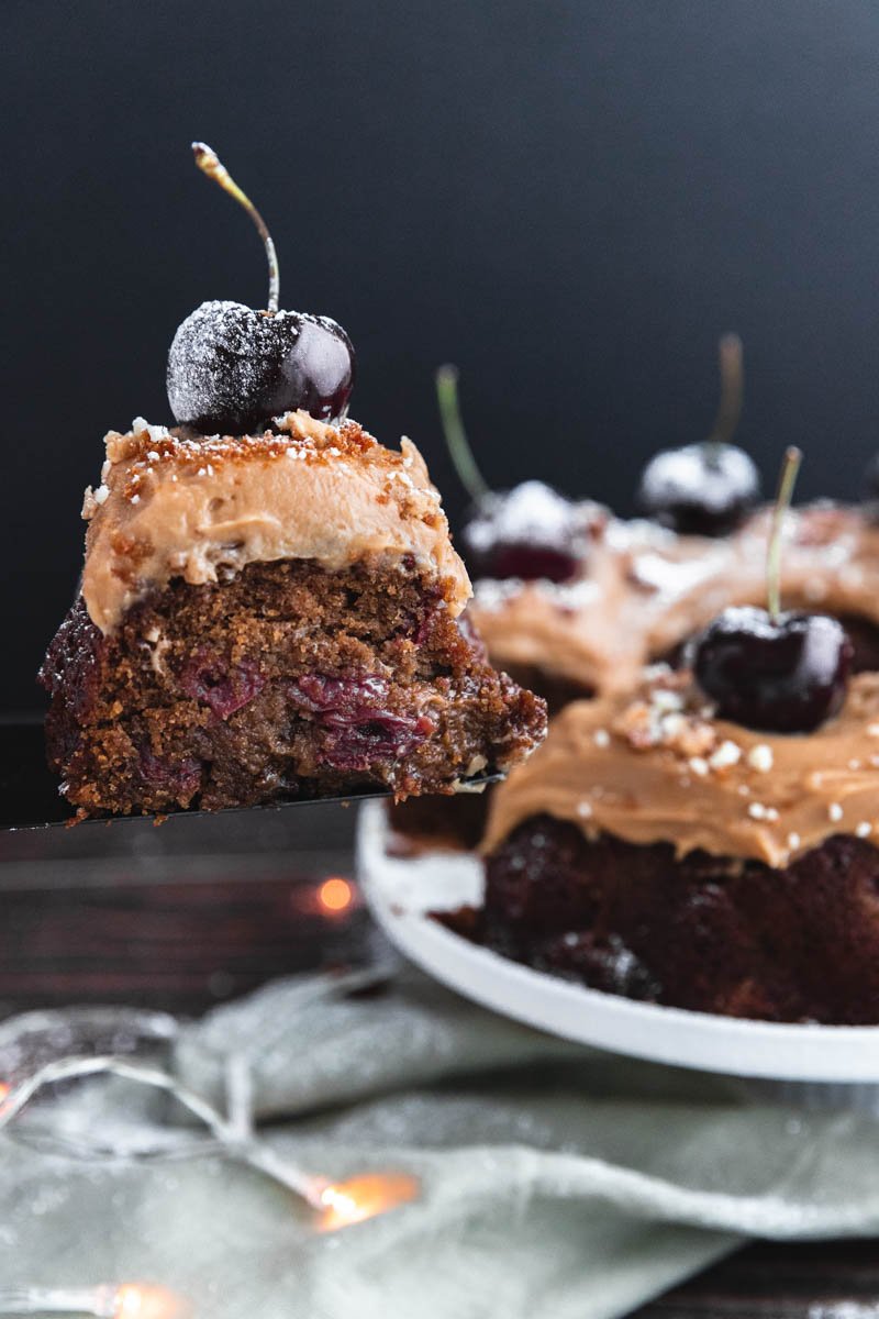 Slice of chocolate cherry cake topped with a cherry and powdered sugar.