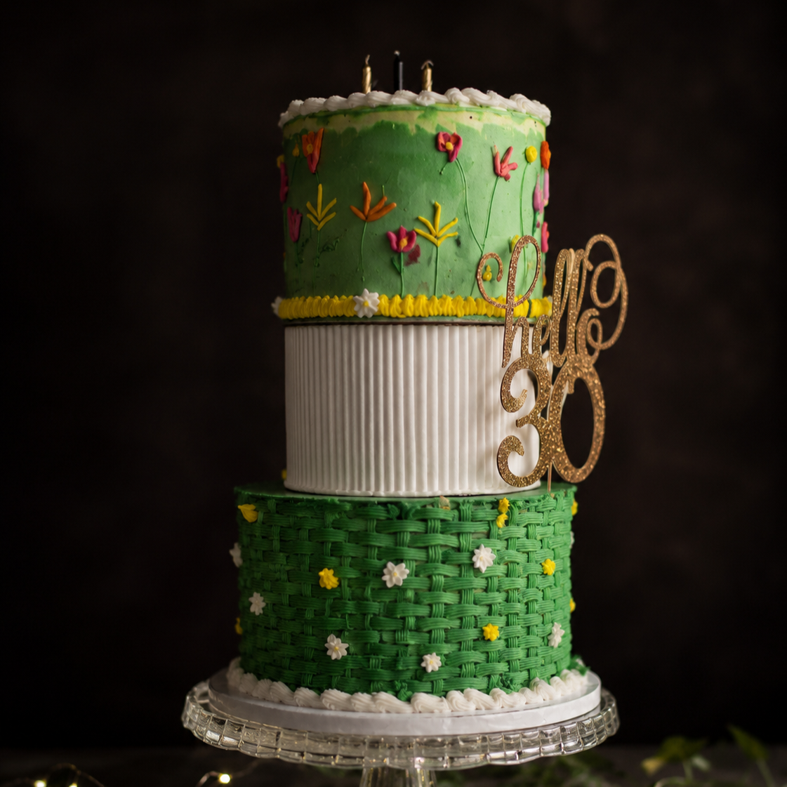 Three-tier green, white, and gold 30th celebration cake with floral accents.