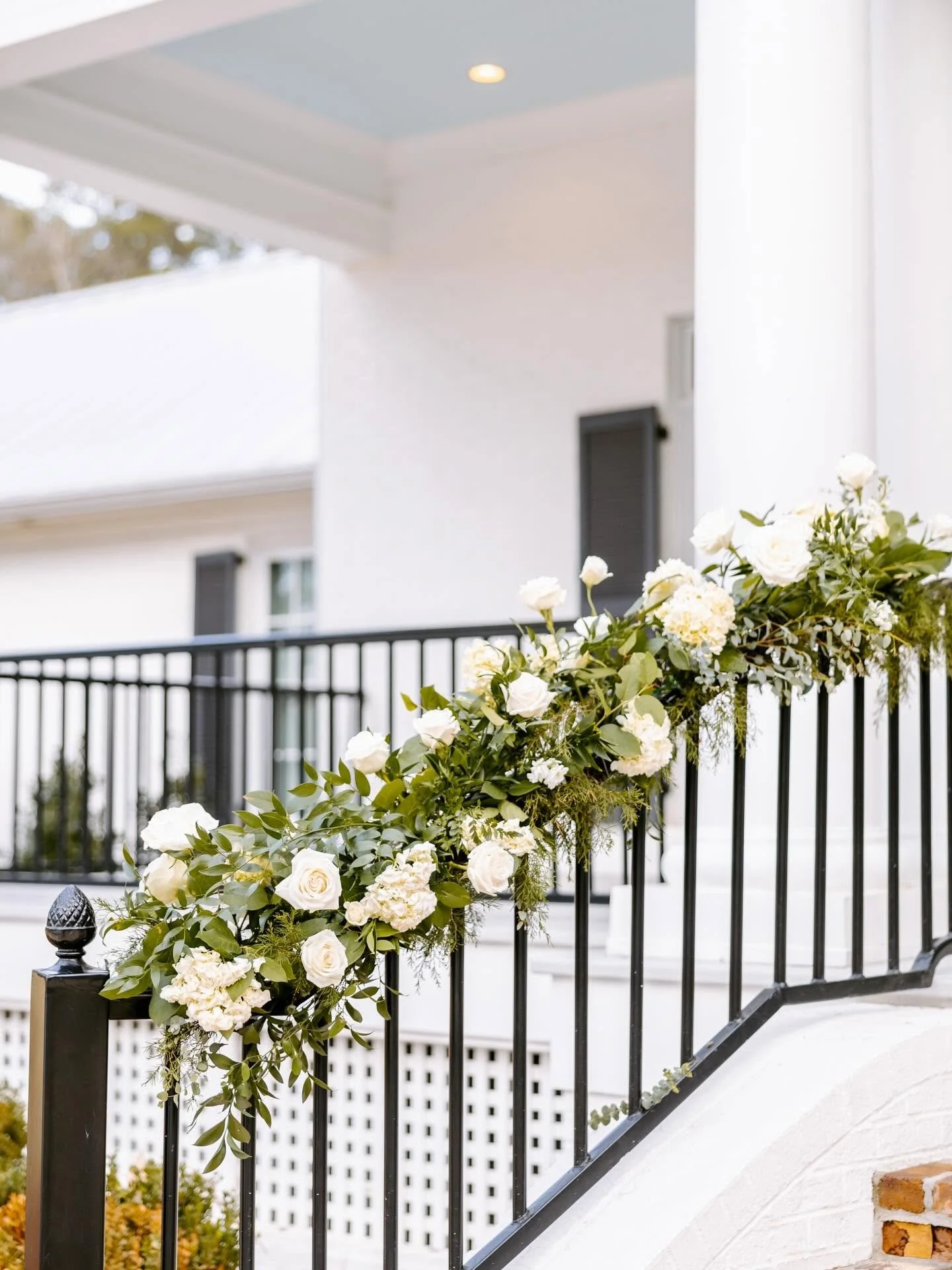 Black metal railing decorated with white roses and green foliage on a porch or balcony.