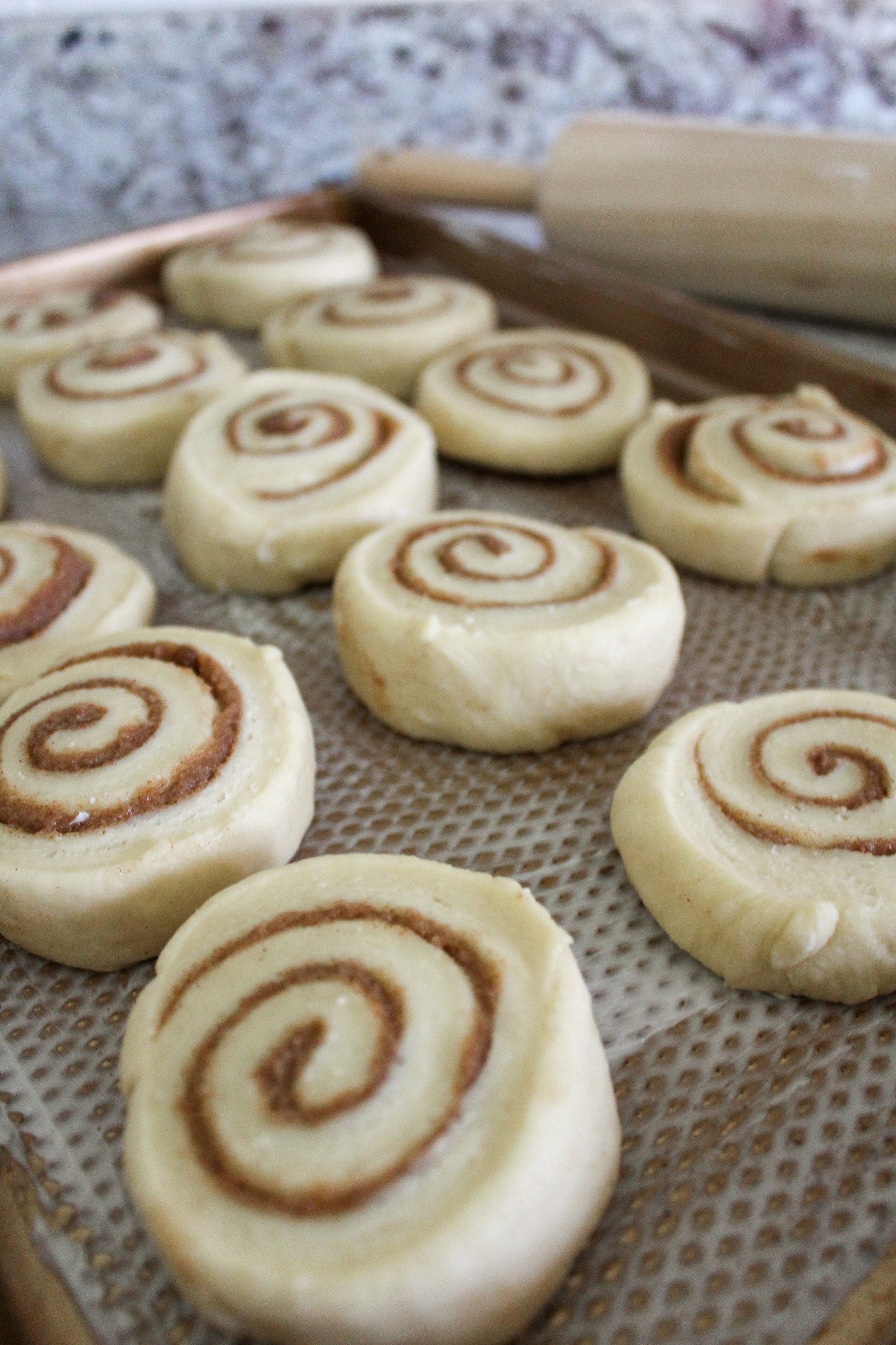 Unbaked cinnamon rolls with cinnamon filling rolled into spiral shapes on a baking sheet lined with parchment paper.