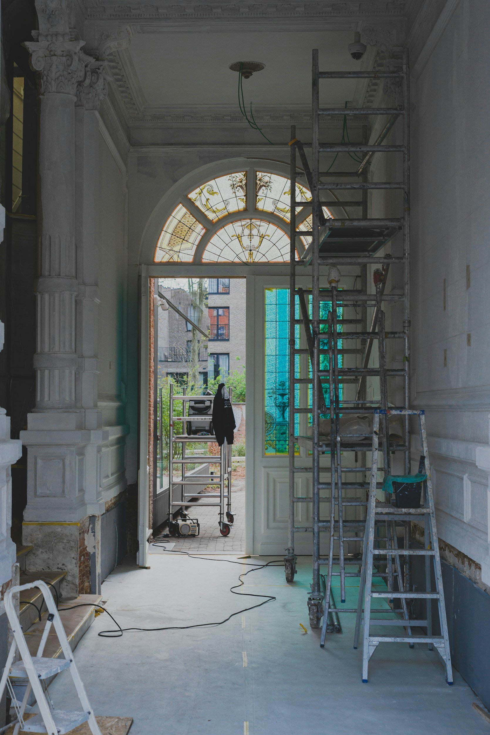 Interior of a building under renovation with scaffolding, a large stained-glass window, construction tools, and electrical wiring visible.