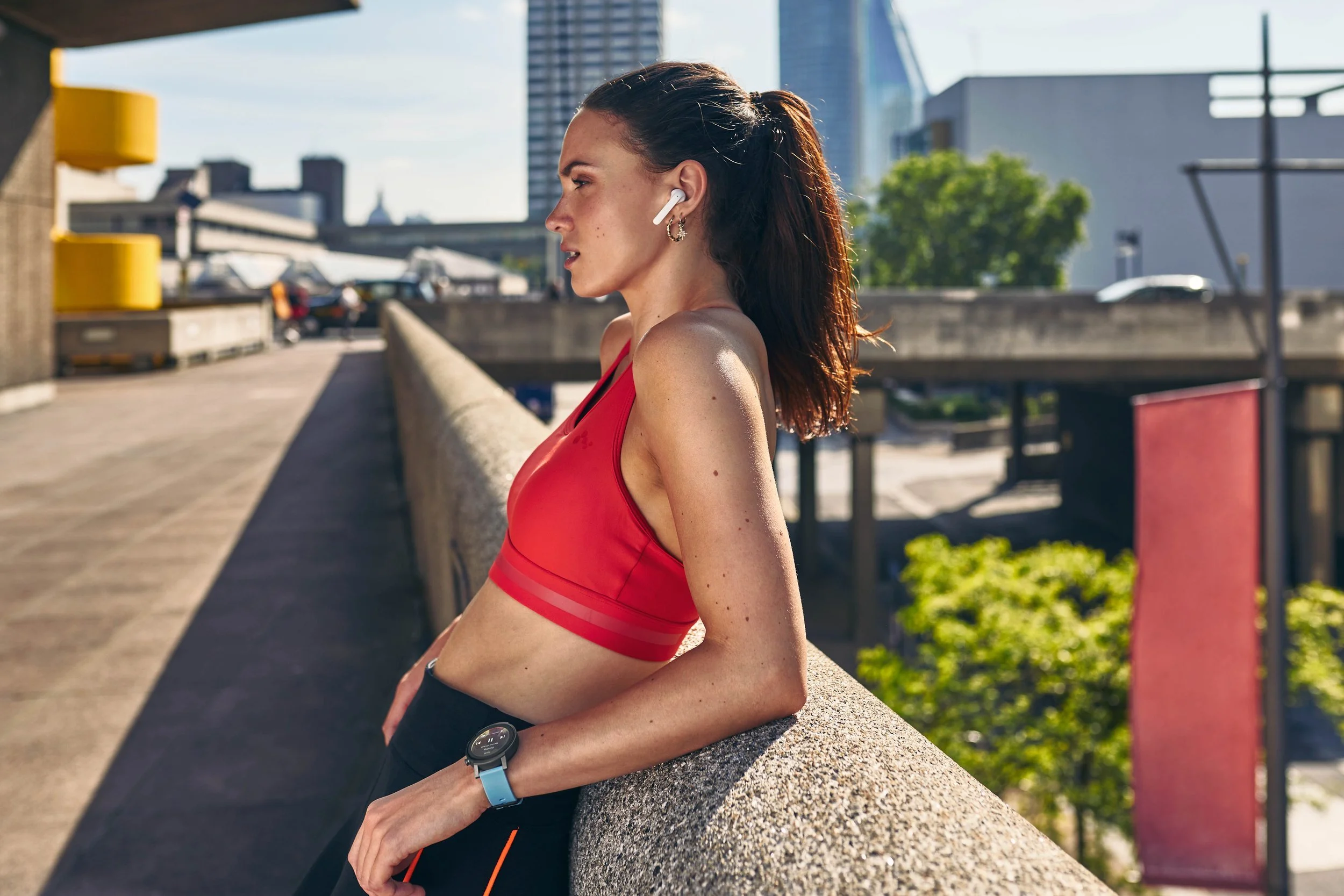 A women stands in the city, headphone in her ears listening to music controlled from her smart watch. Image by sports photographer Jon Enoch