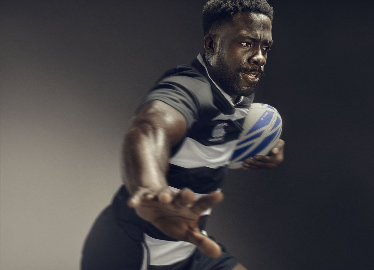 A rugby player hands off the camera in this sports action photography from advertising photographer Jon Enoch