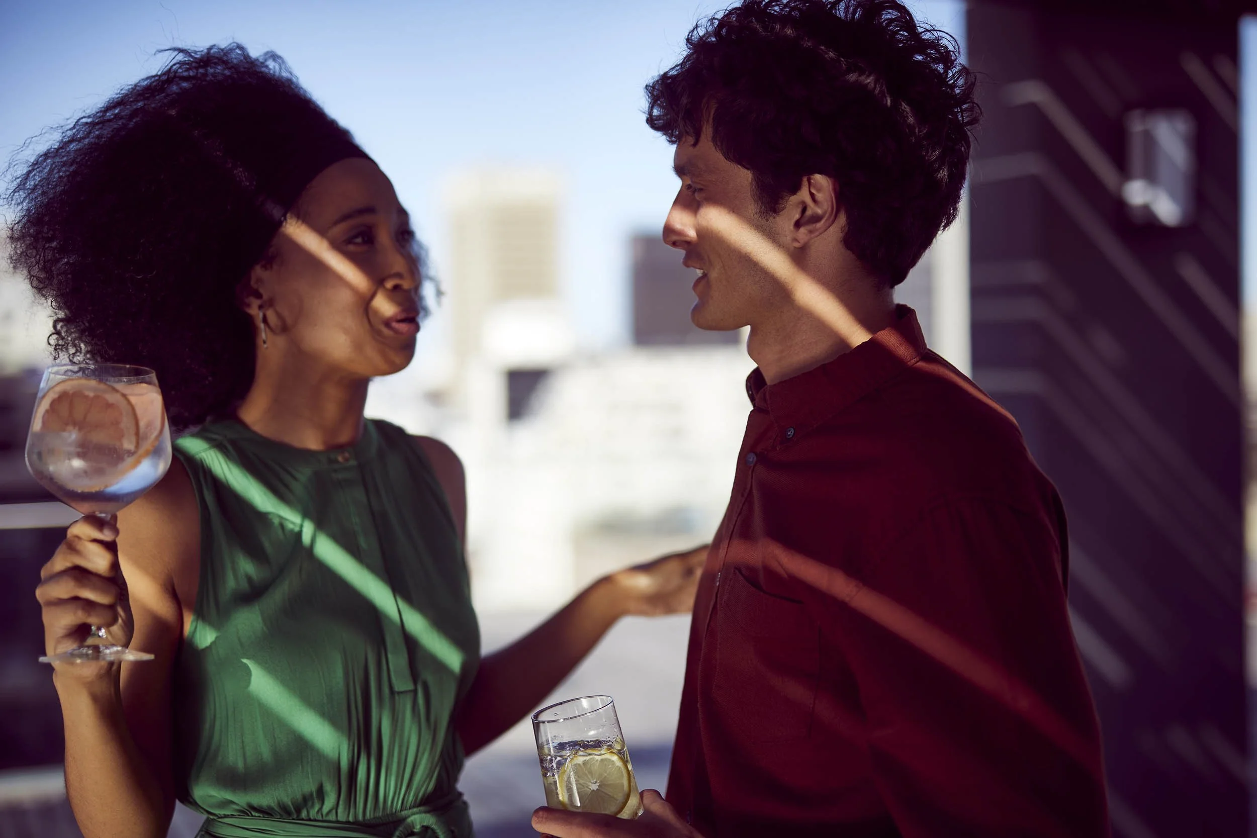 wo friends chat - drinks in hand - as they enjoy the late summer sun on a rooftop in this lifestyle image by Jon Enoch