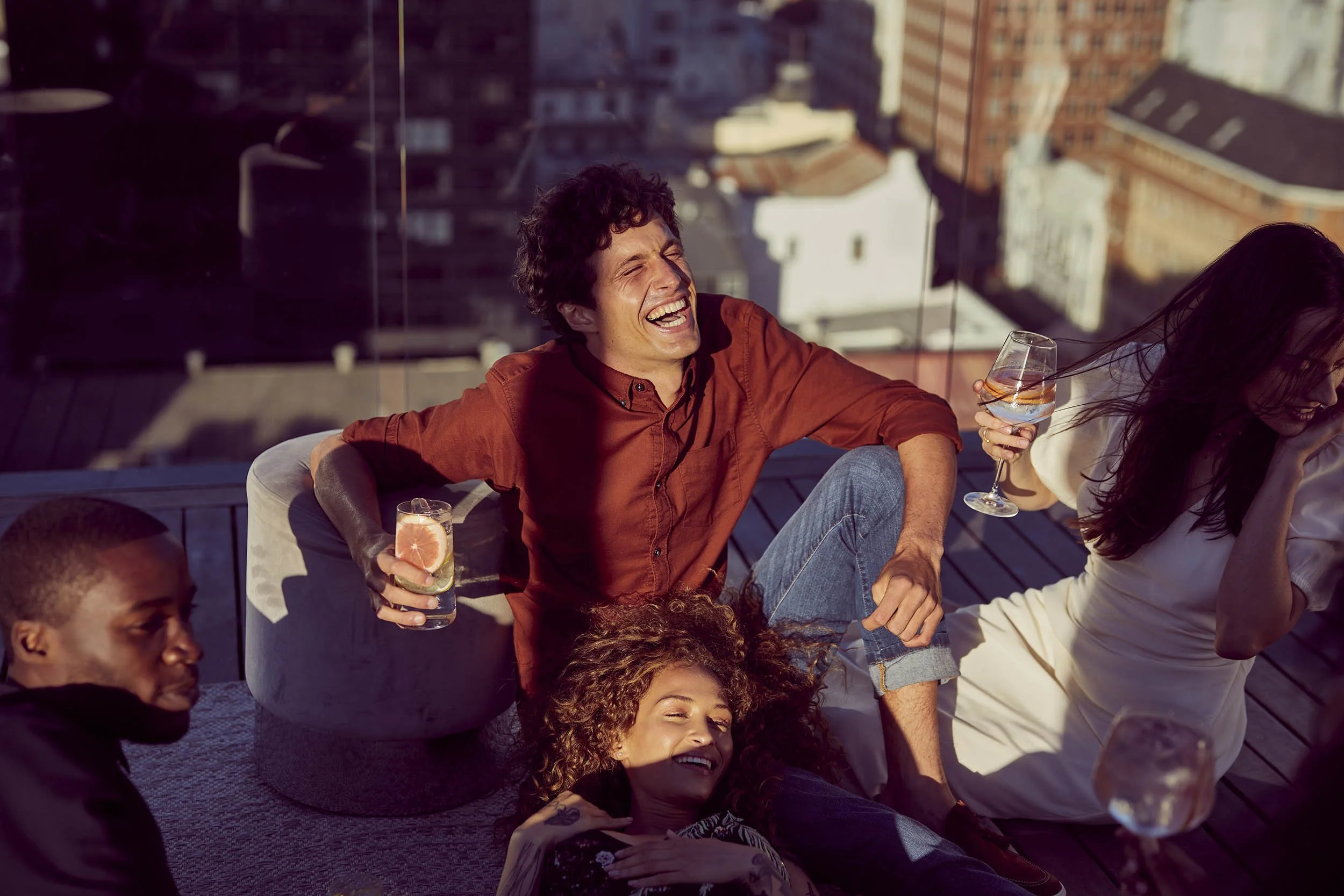 A group of friends drink summer drinks on a rooftop as the golden summer light hits them in this lifestyle image by Jon Enoch