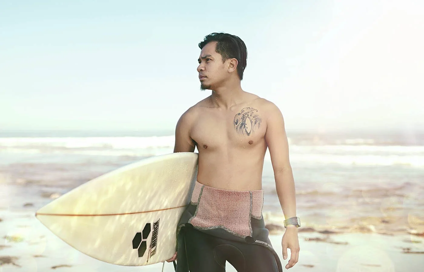 A surfer poses for a portrait before entering the water with his surf board, California, USA. Taken by lifestyle photographer Jon Enoch.
