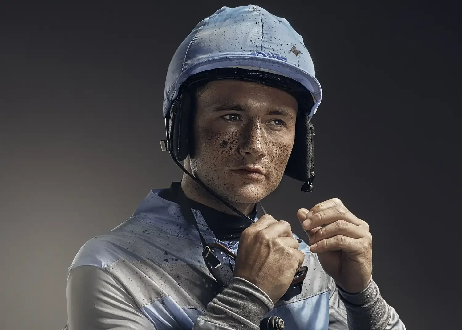 A jockey photographed moments after competition, with mud-stained racing silks reflecting the physical demands of professional horse racing. The image captures the determination, resilience and focus required to perform in one of sport's most challen
