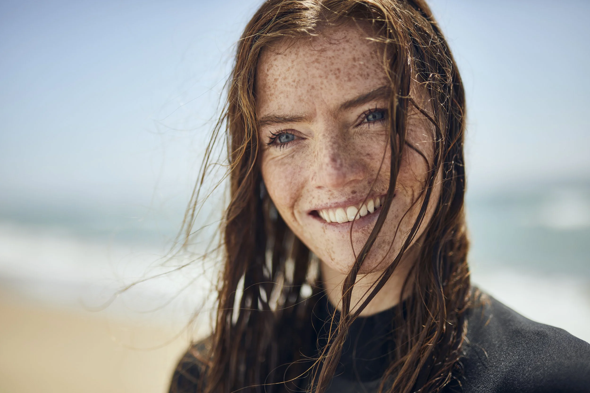 A women in a wetsuit smiles after emerging from the water after a surf on Bournemouth beach, UK. Photographed by lifestyle Photographer Jon Enoch (Copy)