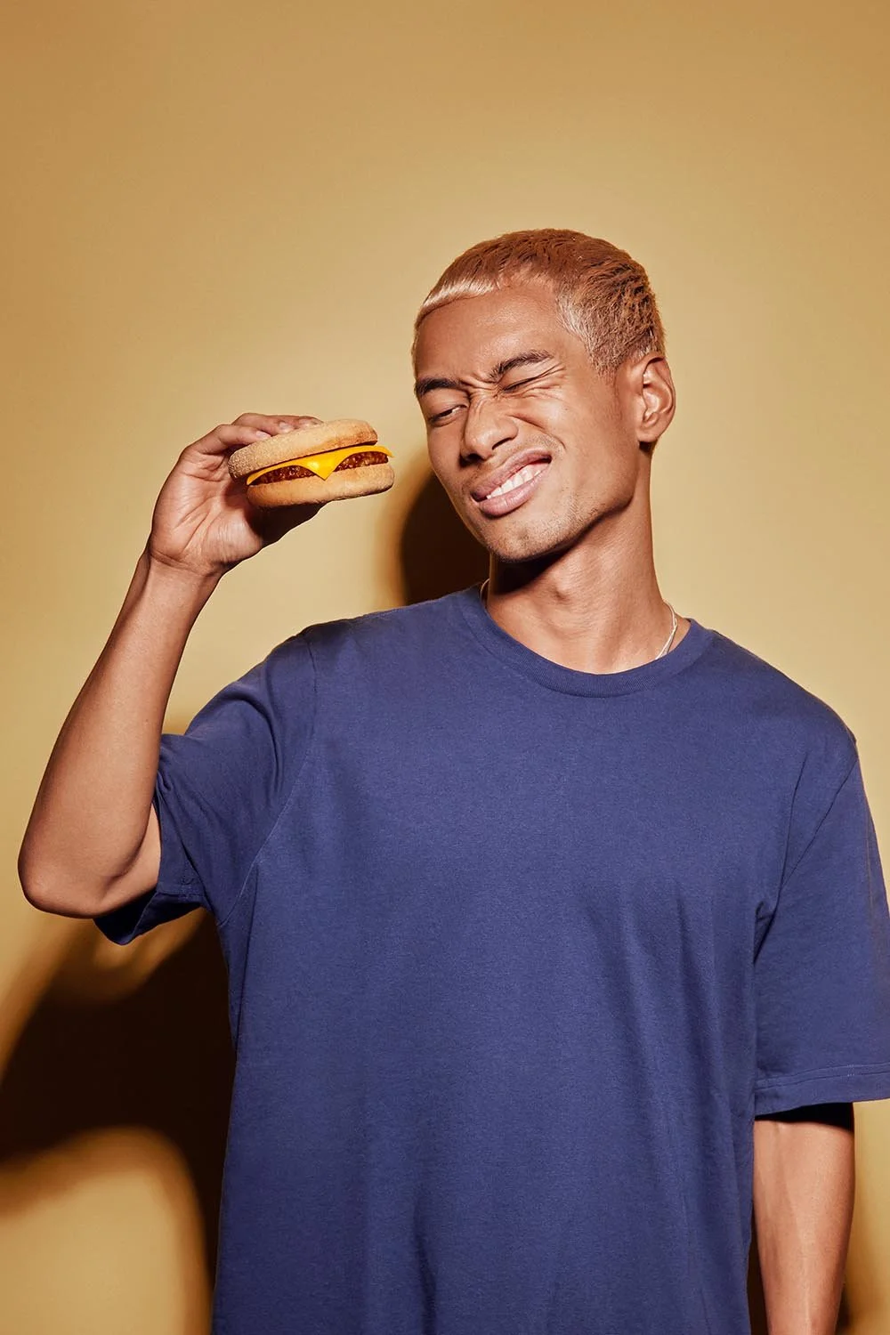 A young man pulls a quirky face whilst holding a burger. Lifestyle food image by Jon Enoch