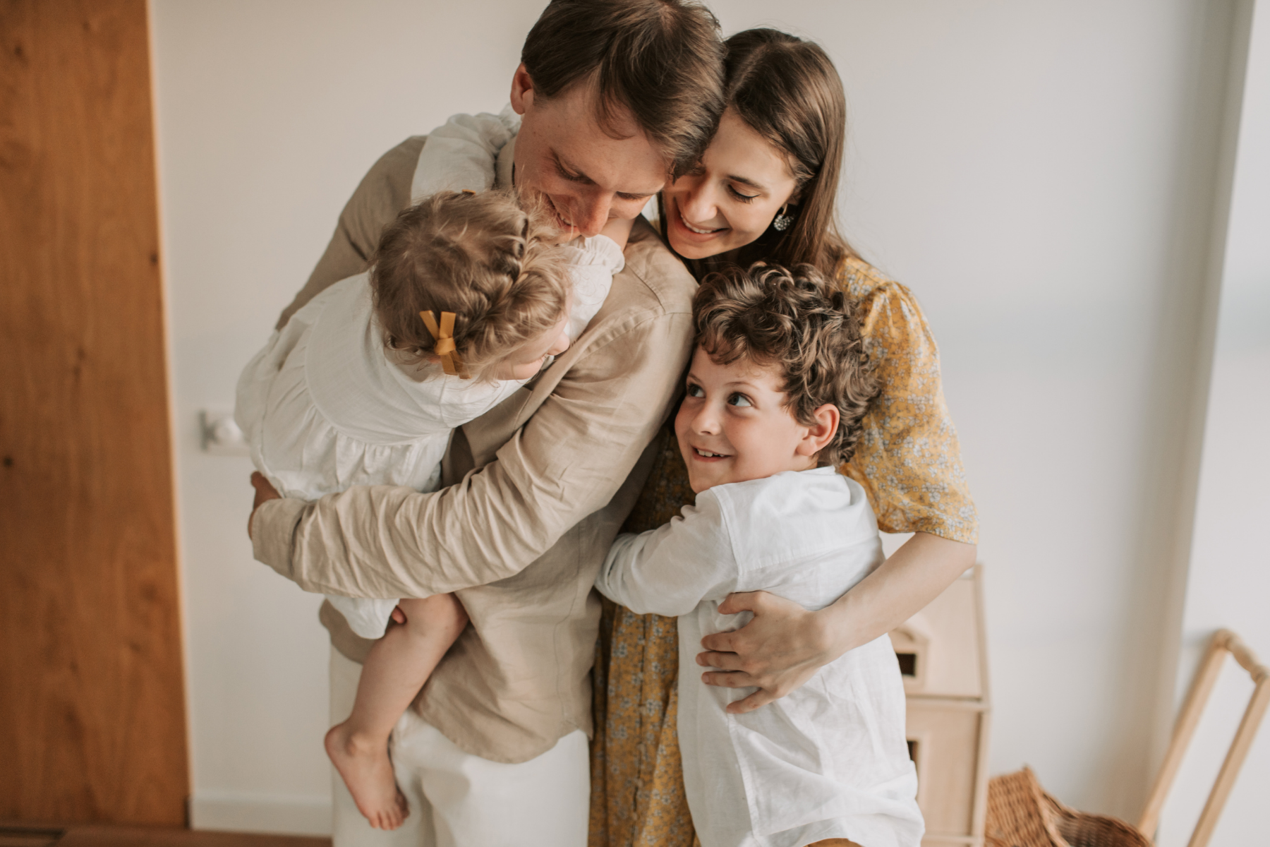 A family of four embracing each other happily inside a home.