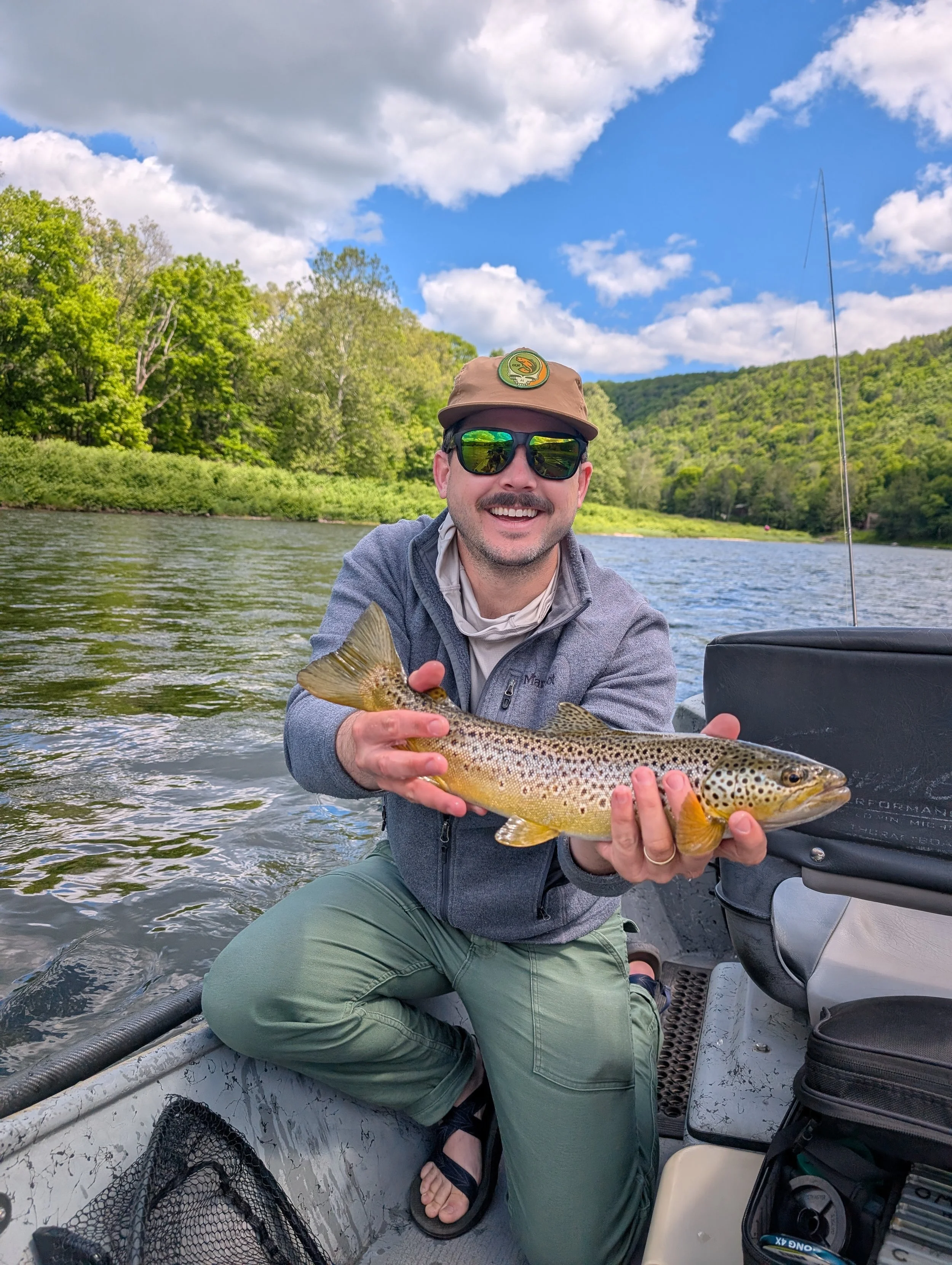 A man in sunglasses and a hat on a boat, holding a large fish he caught.