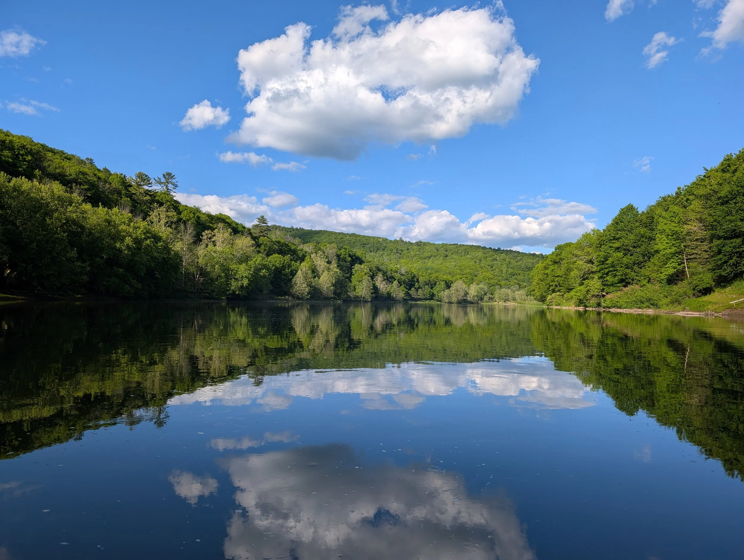 A mirrored stream, calm and still in the bright blue afternoon sky.