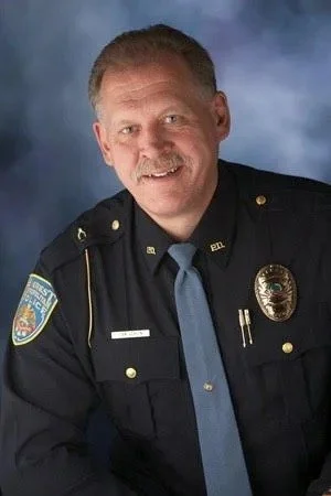 Portrait of a smiling police officer in uniform against a cloudy blue background.