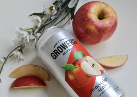A can of Growers honeycrisp apple flavored sparkling water surrounded by fresh apple slices and a whole apple on a white surface.