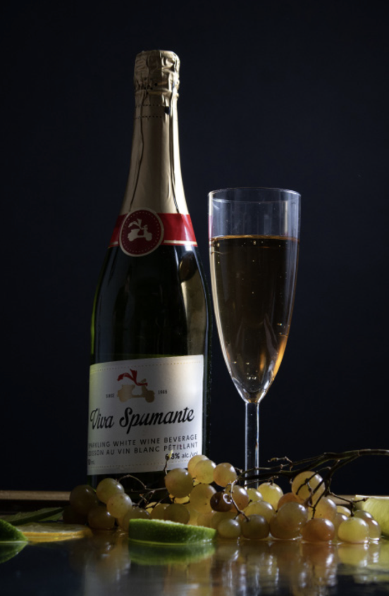 A bottle of sparkling wine, a filled champagne flute, green and white grapes, and lime slices on a reflective surface against a dark background.
