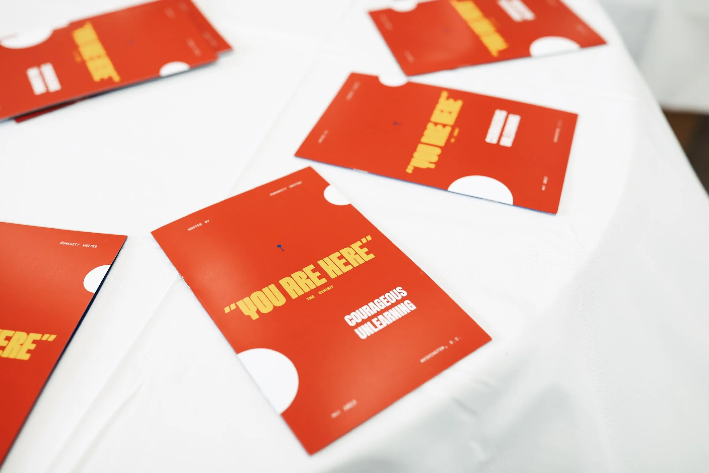 Several red cards with yellow text on a white surface. The cards display motivational phrases such as "You Are Here" and "Courageous Unlearning."