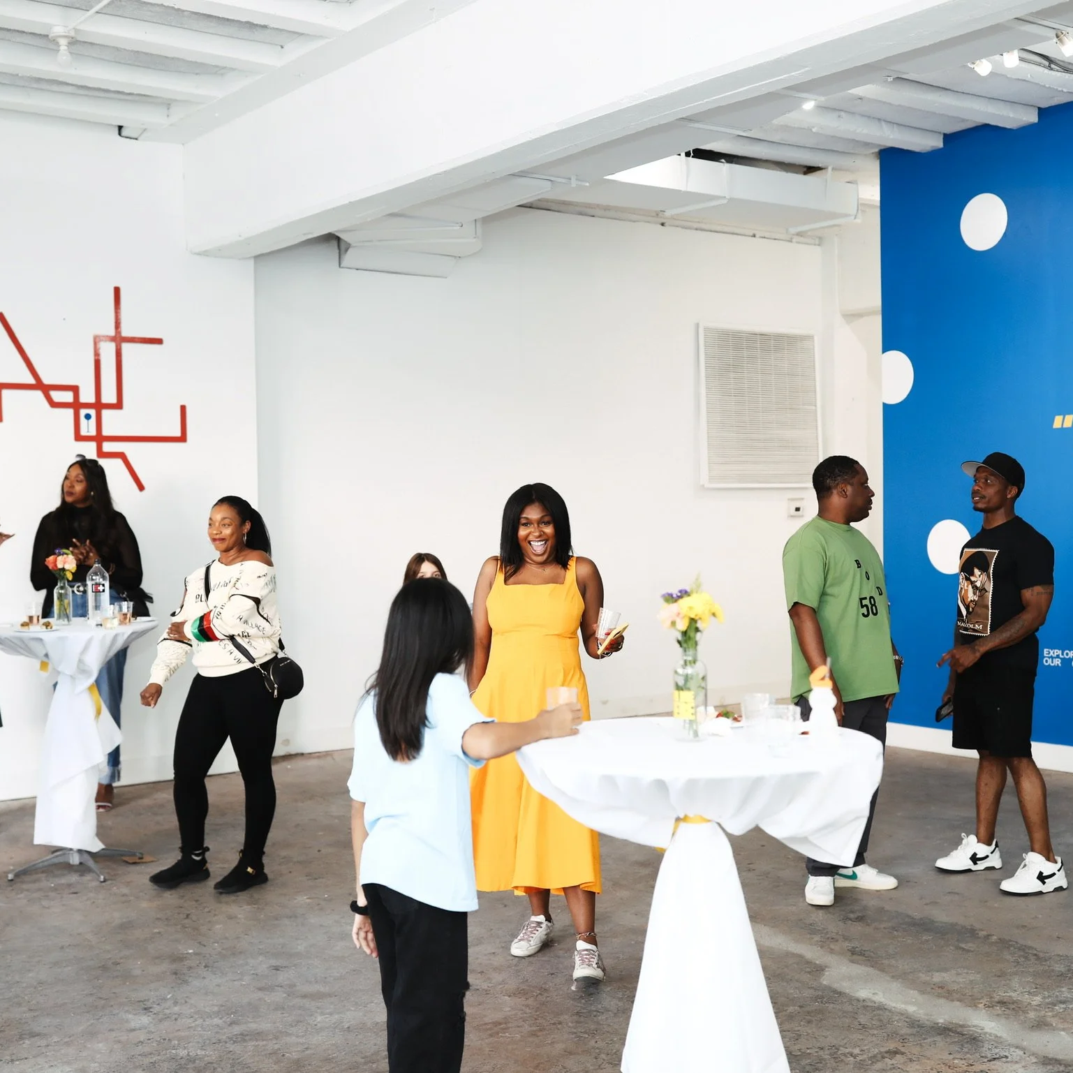People mingling at a social event with arranged tables and vibrant decor.