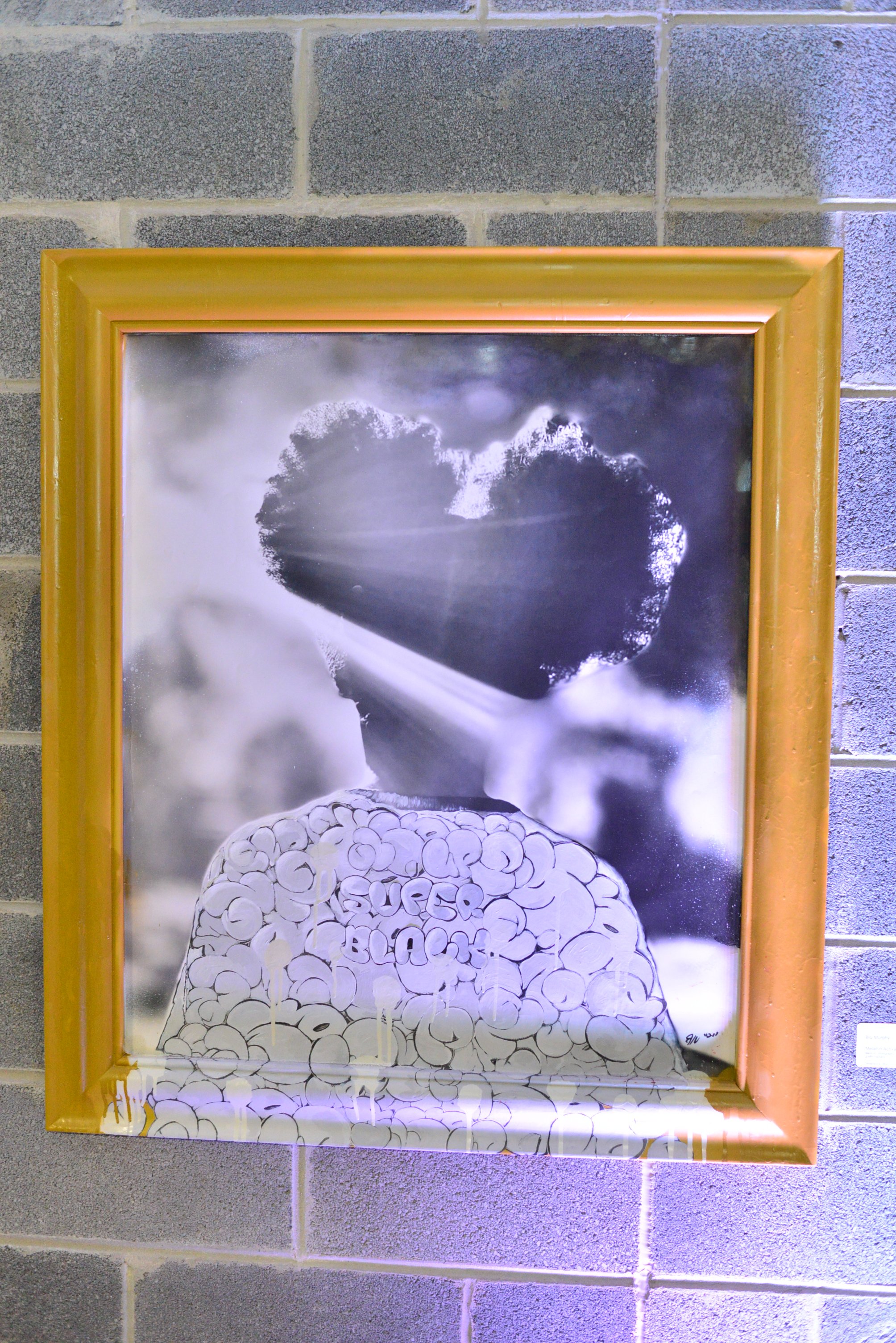 A framed black and white artwork depicting a person with curly hair, with the words 'QUER BLAN' inside the hair, set against a background of clouds and light rays.