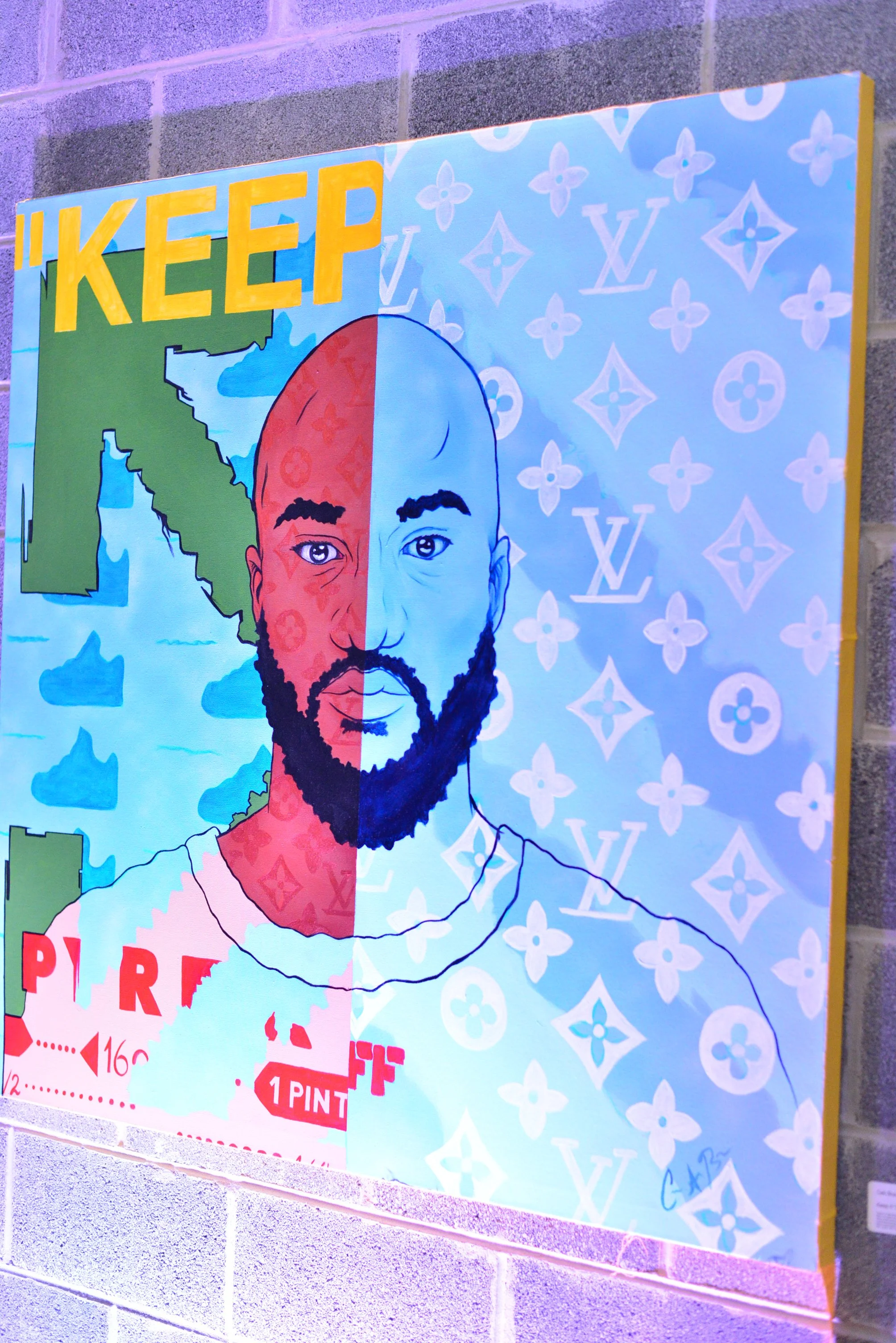 A colorful poster featuring a stylized illustration of a man with a beard, divided into two halves with different backgrounds. The left half shows a map of Italy and the word 'KEEP' in large yellow letters, while the right half has a patterned background with the Louis Vuitton logo. The poster appears to be part of an art display on a concrete wall with purple lighting.