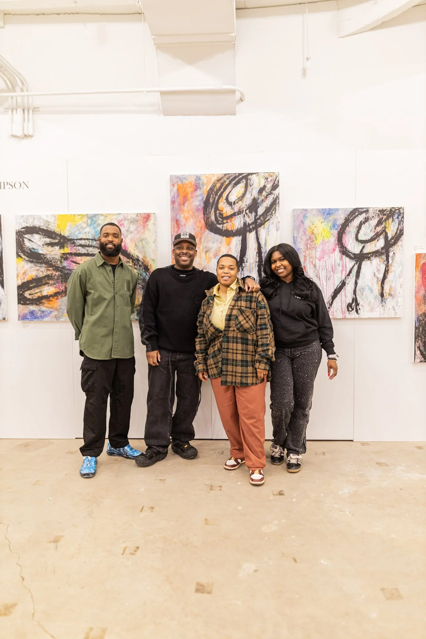 Four people standing in front of abstract artwork in an art gallery or studio. They are smiling and posing for the photo.