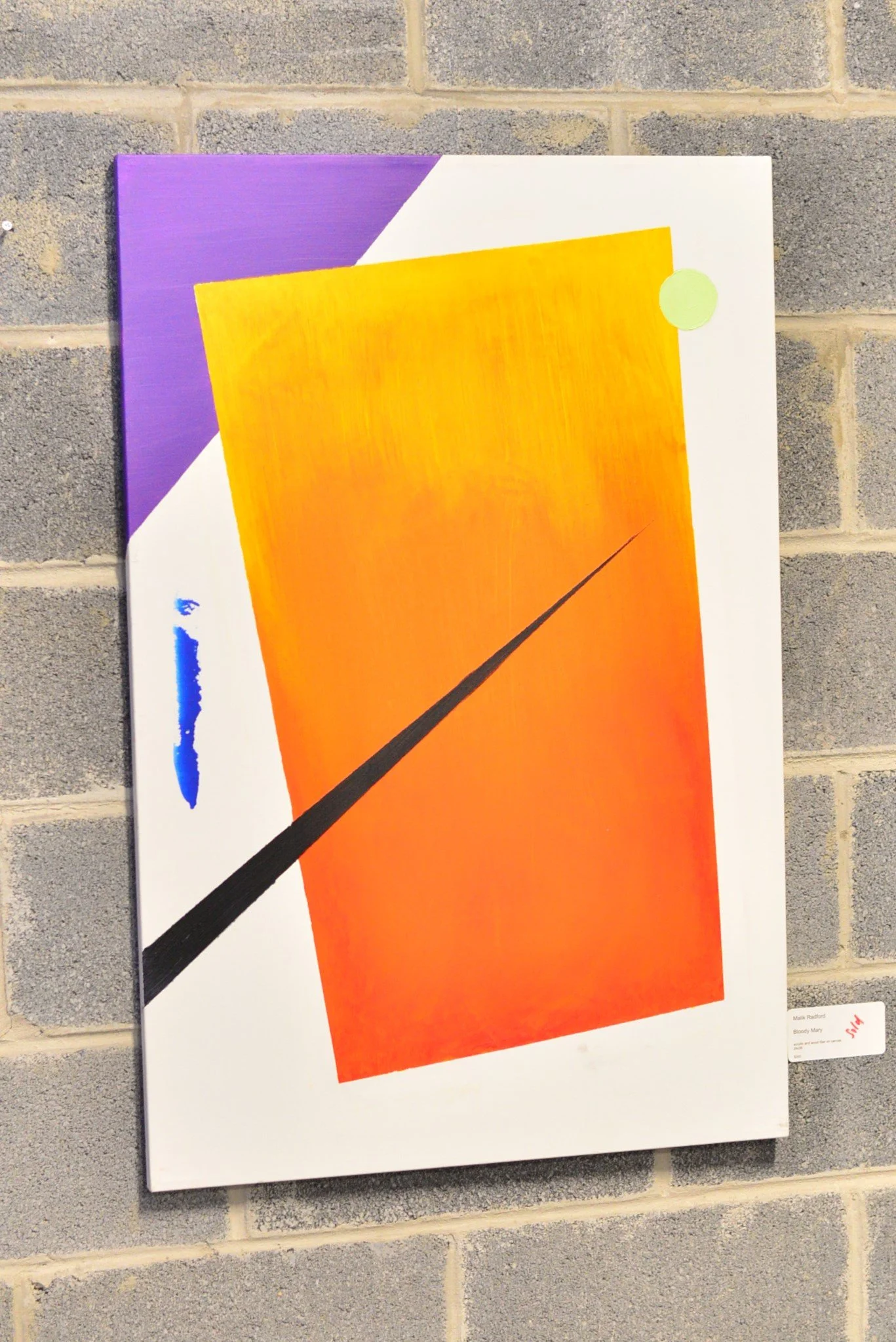 Abstract painting featuring a large orange rectangle with a yellow circle at the top right corner, a black diagonal line crossing from bottom left to top right, with a purple triangle in the upper left corner and a white area in the bottom right corner, displayed on a brick wall.