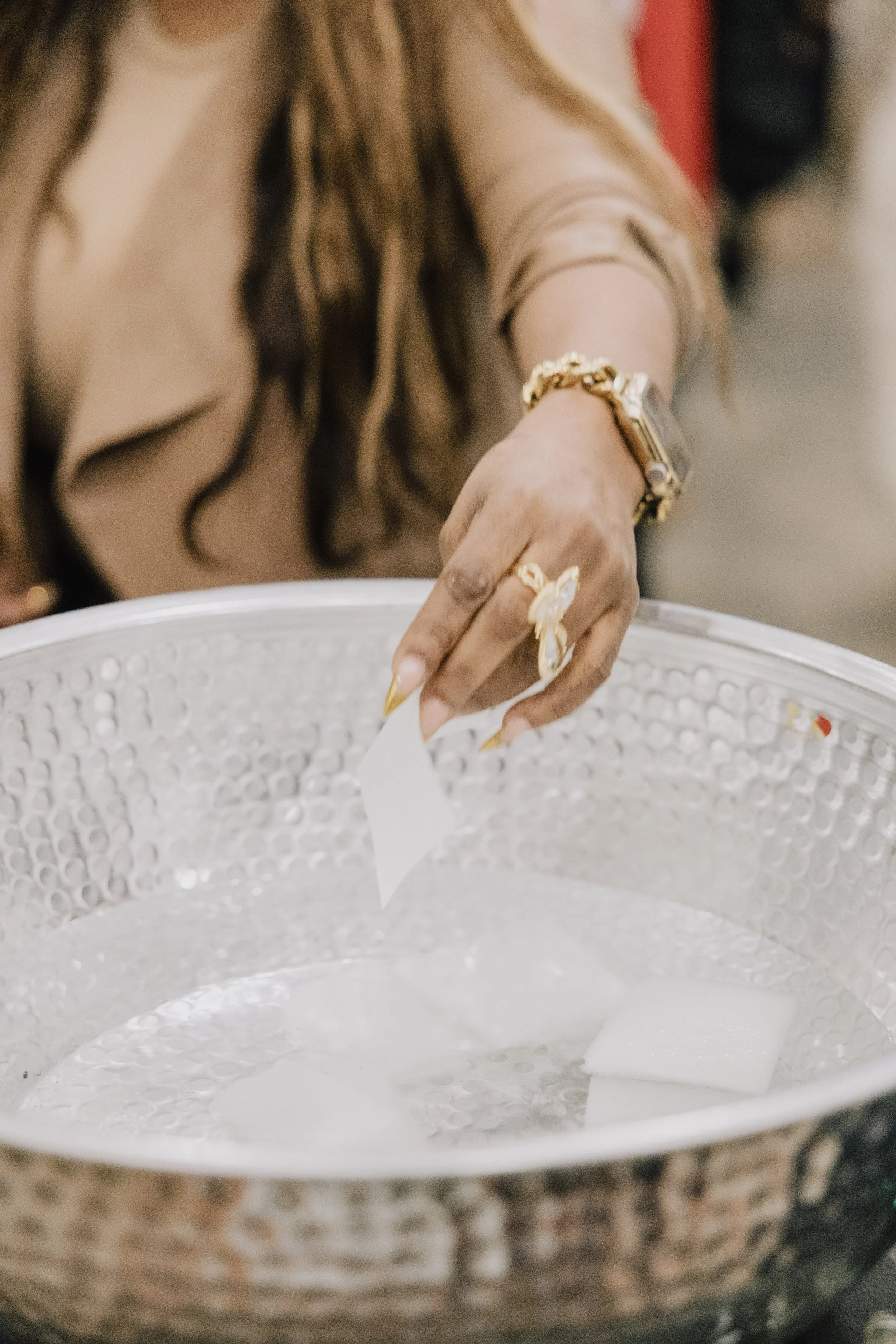 Close-up of a woman's hand with jewelry, reaching into a metallic bowl.