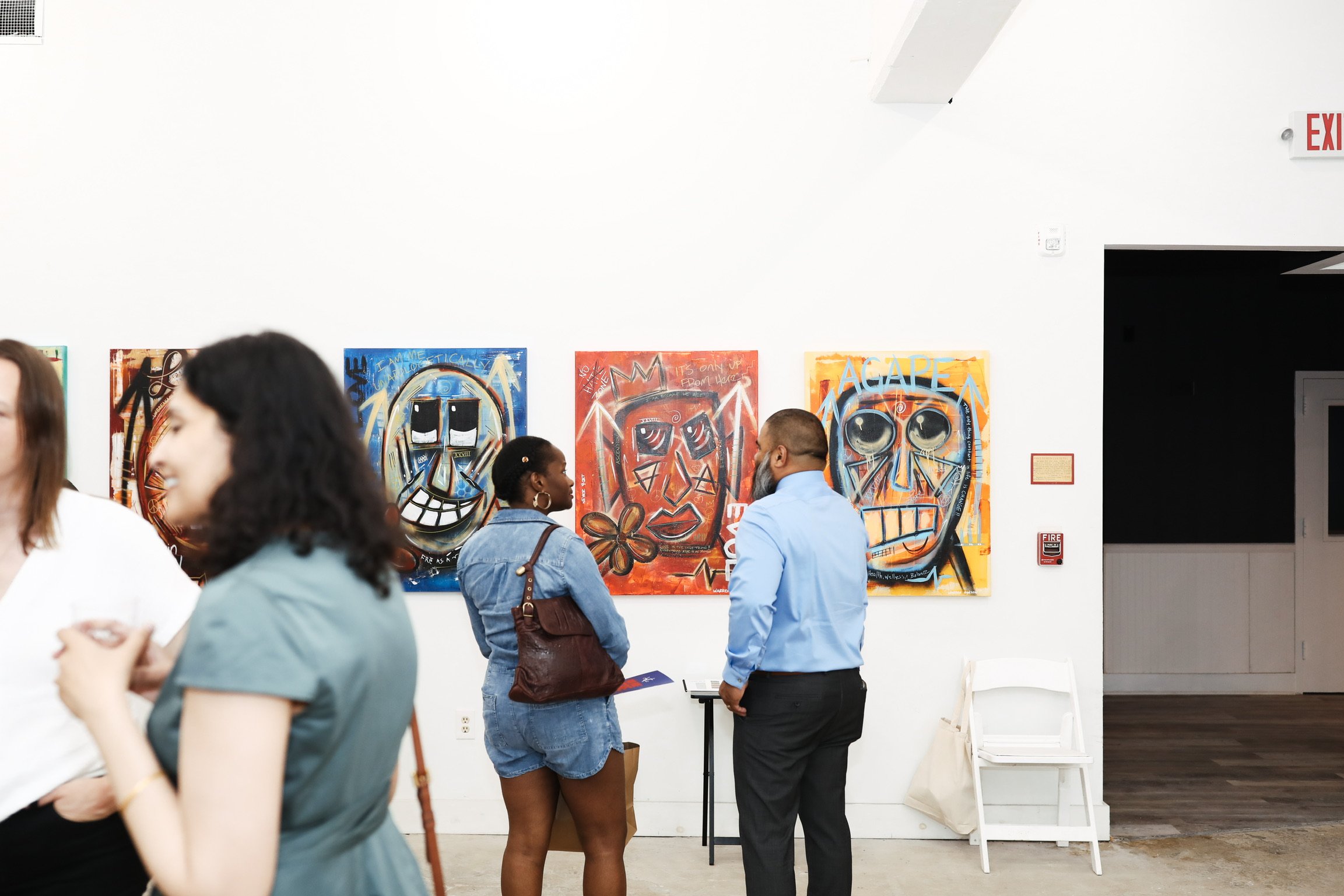 People standing and talking at an art gallery with colorful graffiti-style artwork on the wall.