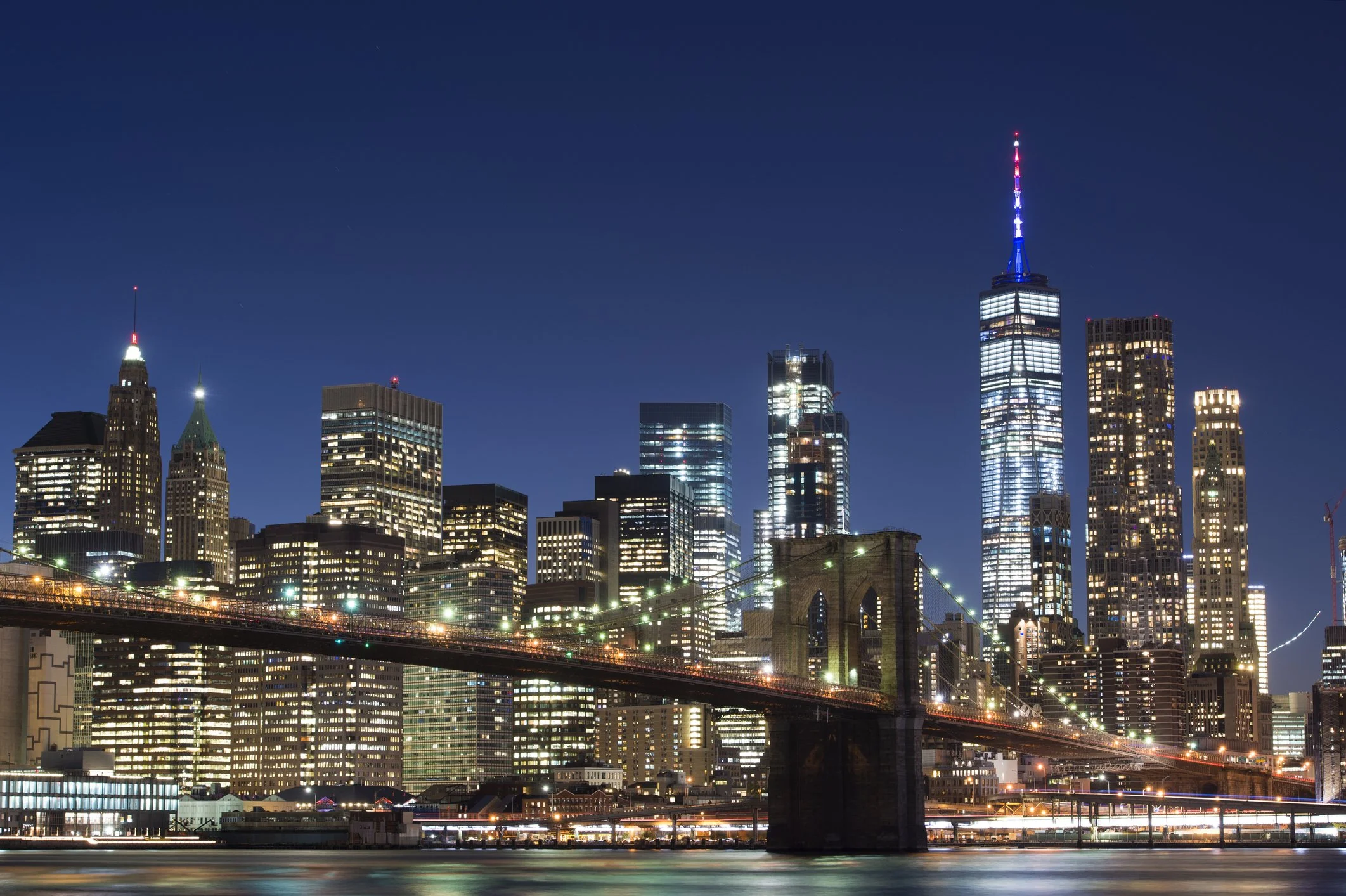 Night view of New York City skyline with illuminated skyscrapers and Brooklyn Bridge.