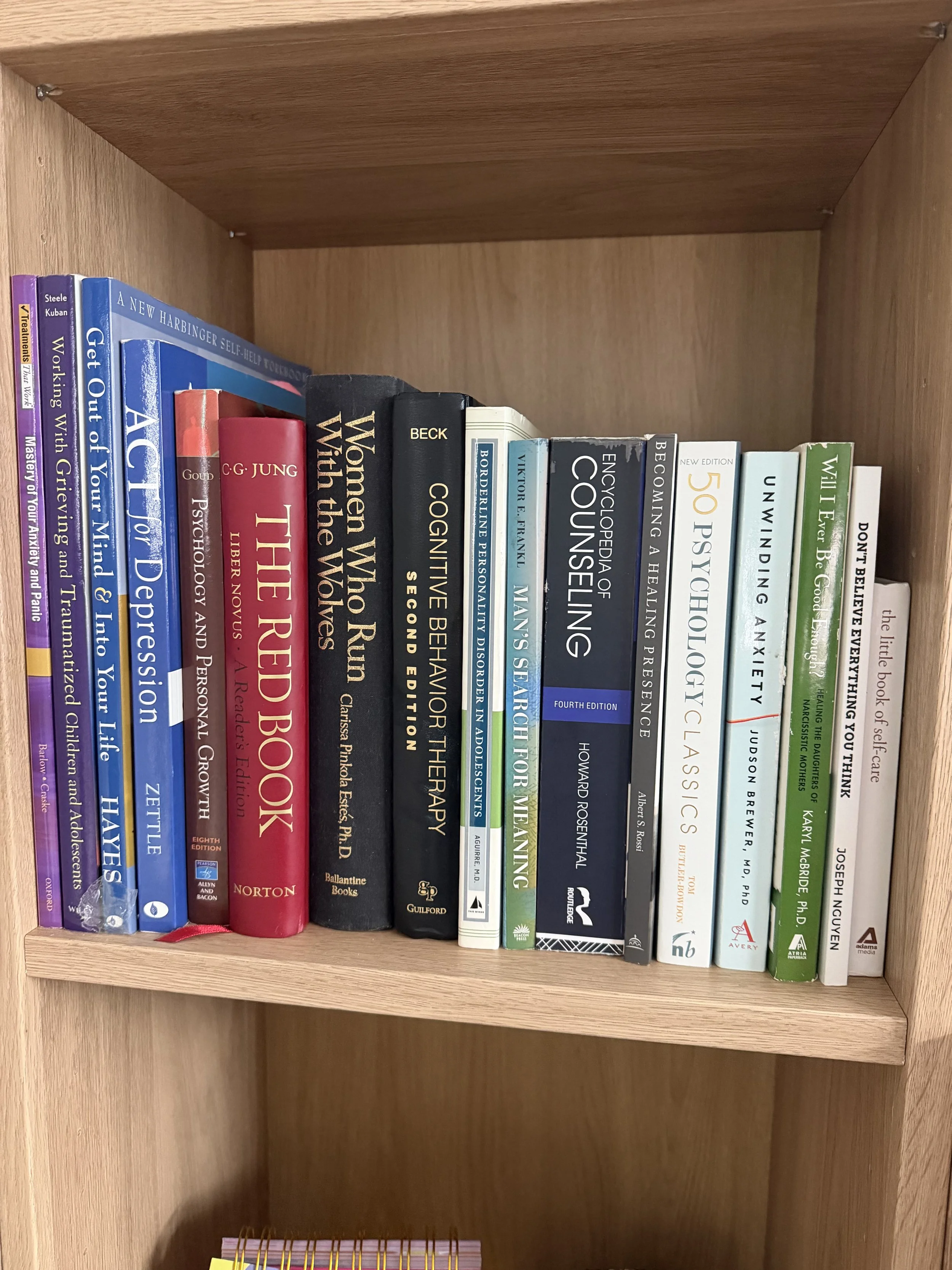 A wooden bookshelf with various books on psychology, therapy, self-help, and personal development, aligned vertically.