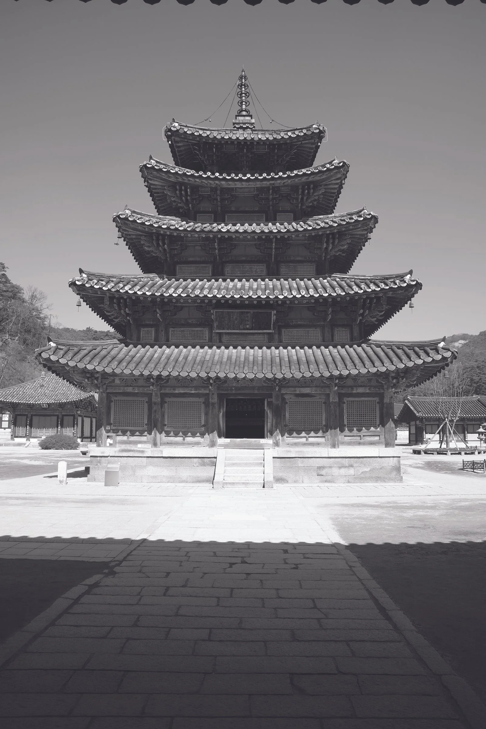 A traditional multi-tiered wooden pagoda with curved eaves, situated outdoors with a wide stone staircase and surrounding buildings.
