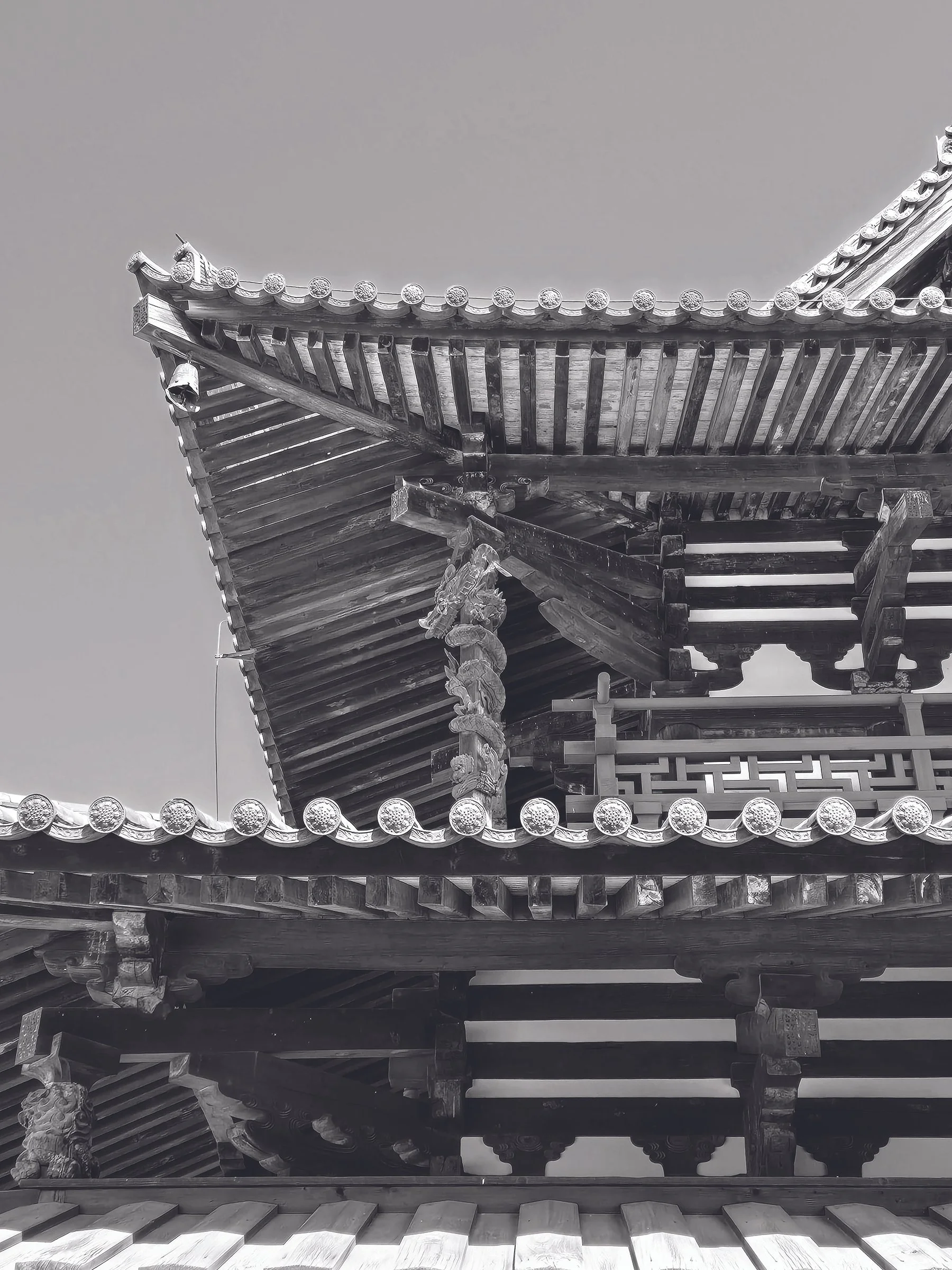 Black and white photograph of the ornate roof of a traditional Asian wooden building, featuring layered eaves, decorative carvings, and ridged tiles.
