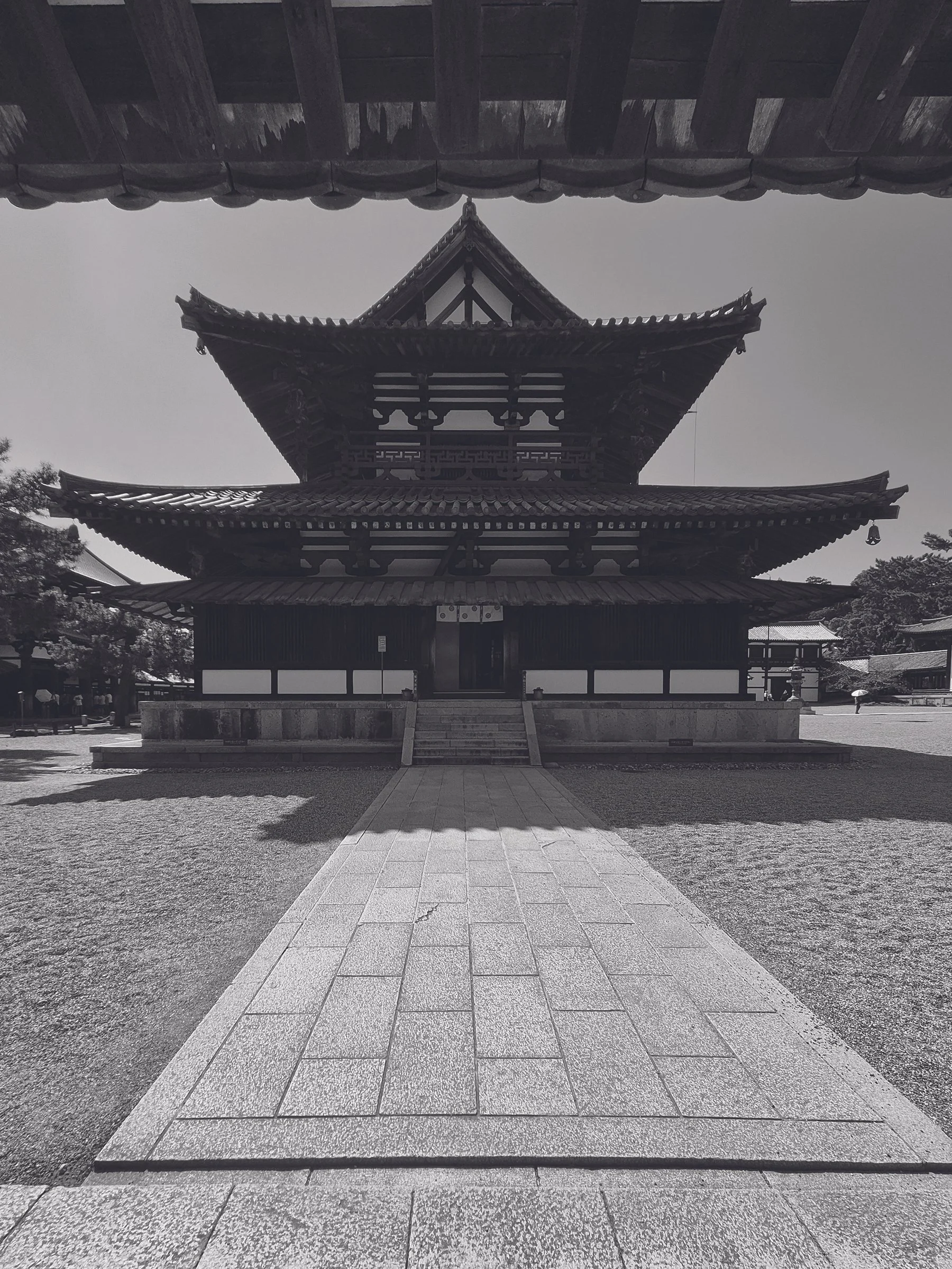 Traditional Japanese wooden temple with curved roof, situated in a courtyard with stone steps and pathway, under a clear sky.