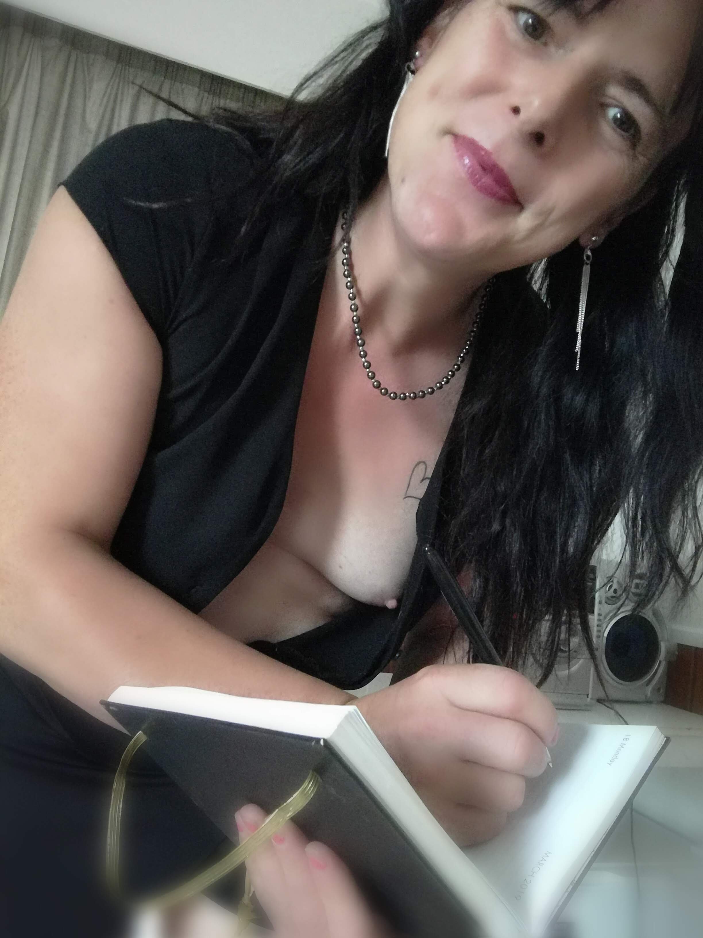 Close-up of a woman with black wavy hair, wearing a black shirt and jewelry, reading a small book or planner.
