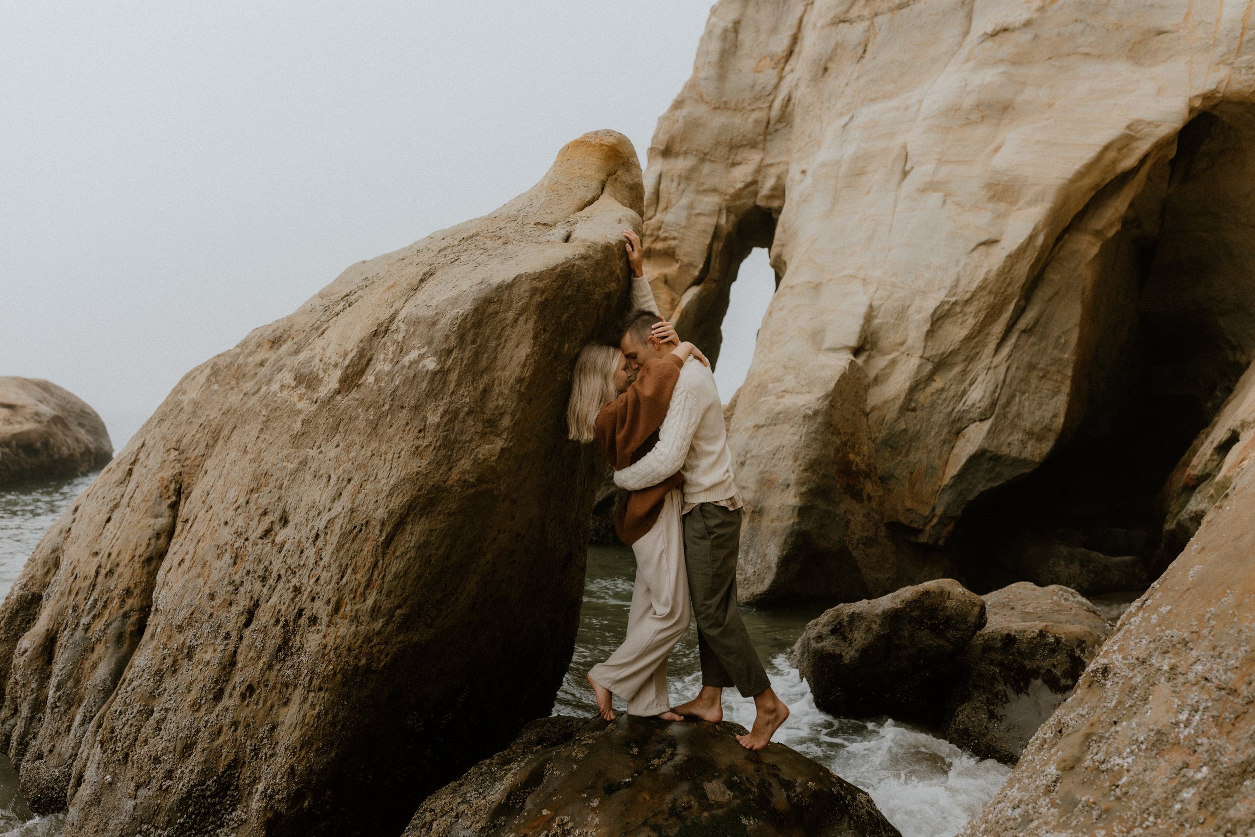 A couple embracing between tall rocks by the water