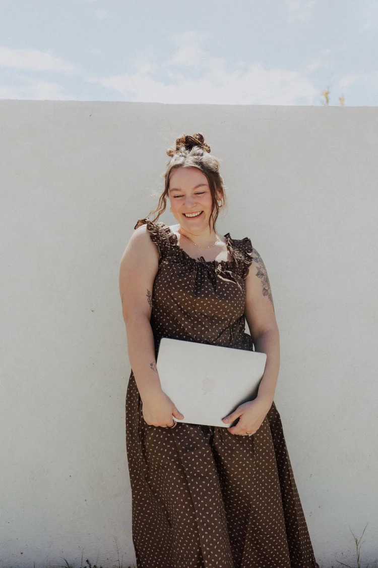 Calle Morain smiling with her laptop against a white wall
