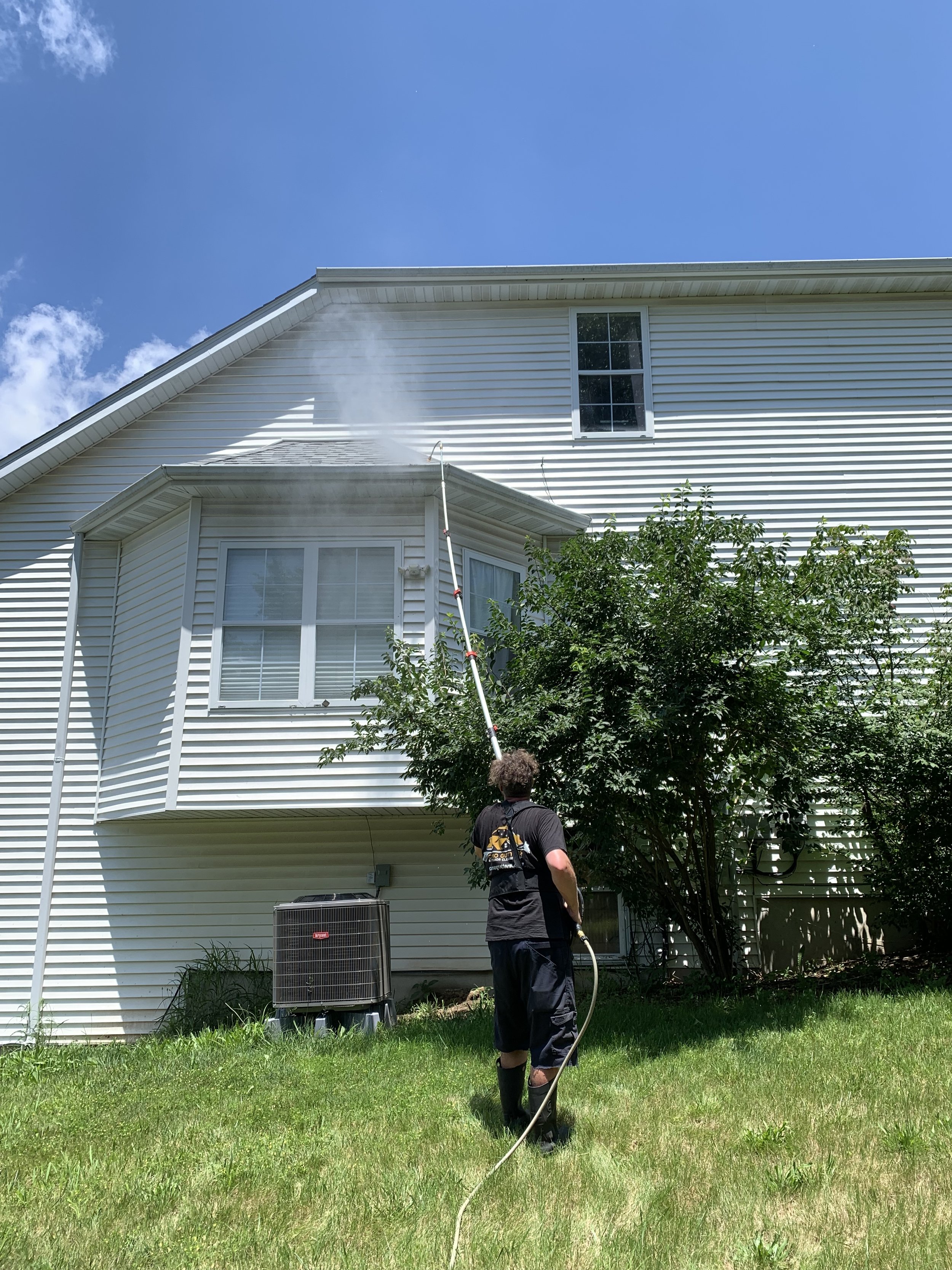 A person using a pressure washer to clean the exterior siding of a house, which has dirt and mold.