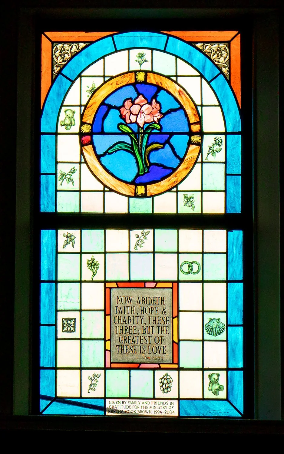 Visually striking stained glass with inscription — “Now abideth faith, hope & charity, these three; but the greatest of these is love”.   The dedication panel at the very bottom reads:
Given by family and friends in
gratitude for the ministry of
Bert