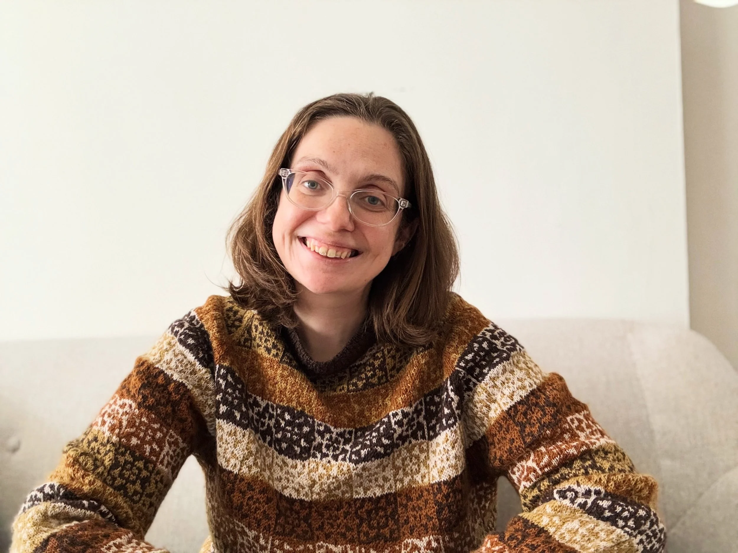 A 30-something white woman in a handknitted sweater smiles at the camera