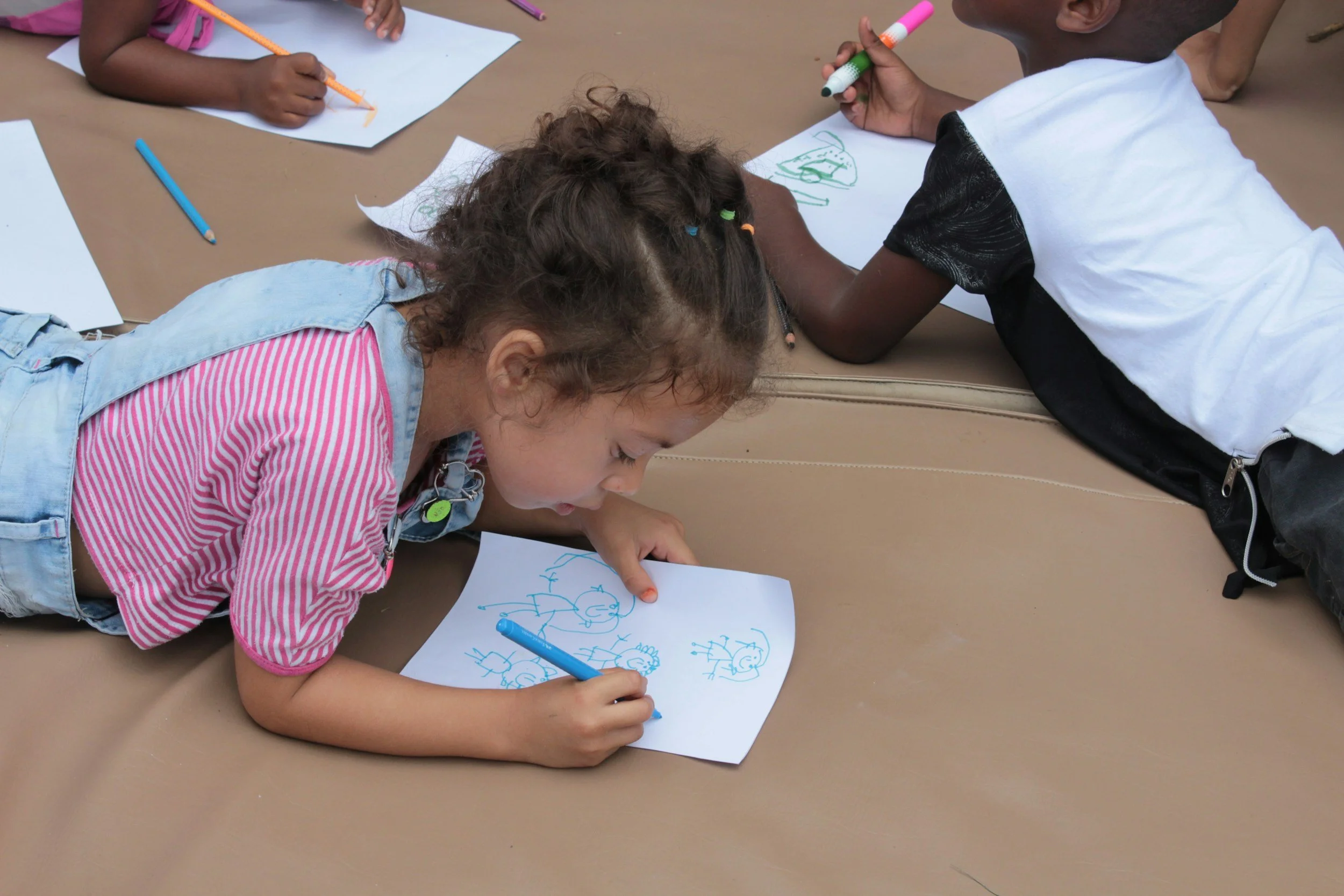 Stock photo image from Unsplash of three children coloring sheets of paper on a blanket on the floor.