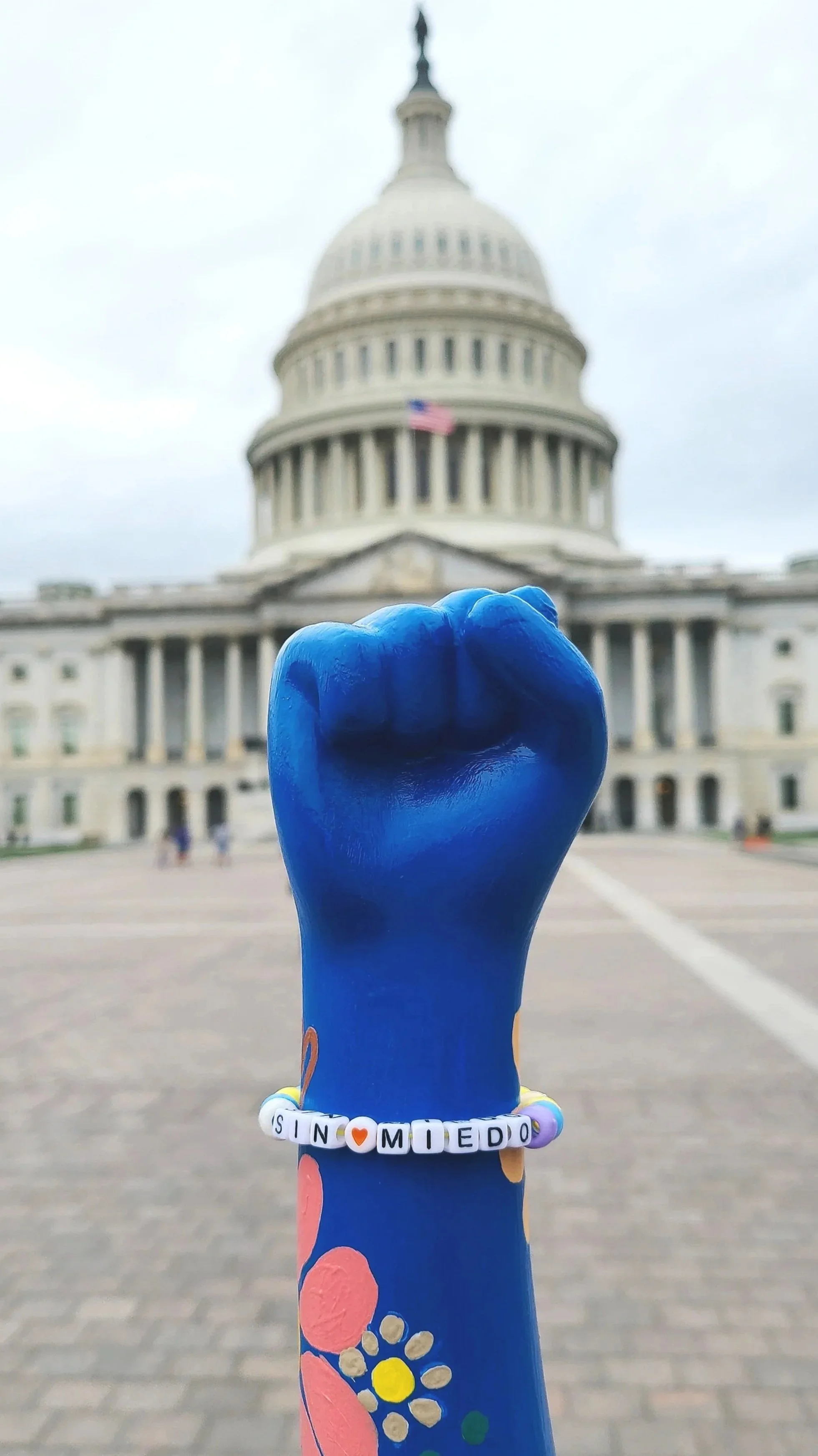 3D sculpture fist painted painted blue with colorful flowers and a beaded bracelet reading "SIN MIEDO" in front of the U.S. Capitol building in Washington, D.C.