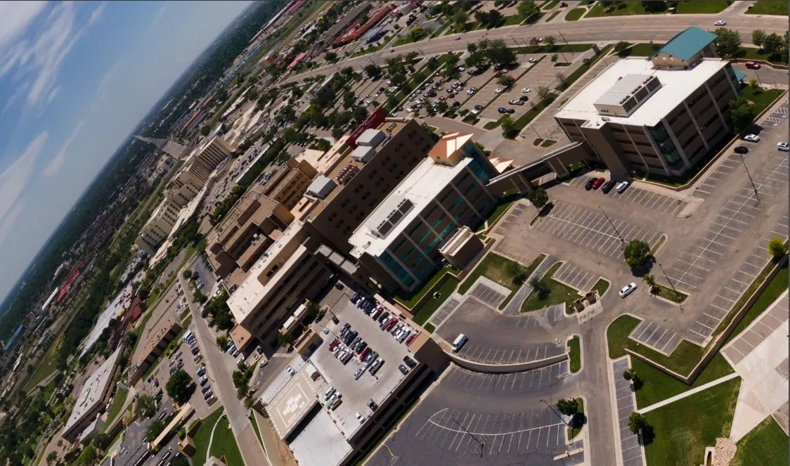 Aerial view of a large parking lot and several modern office buildings in an urban area with a highway and more city structures in the background.