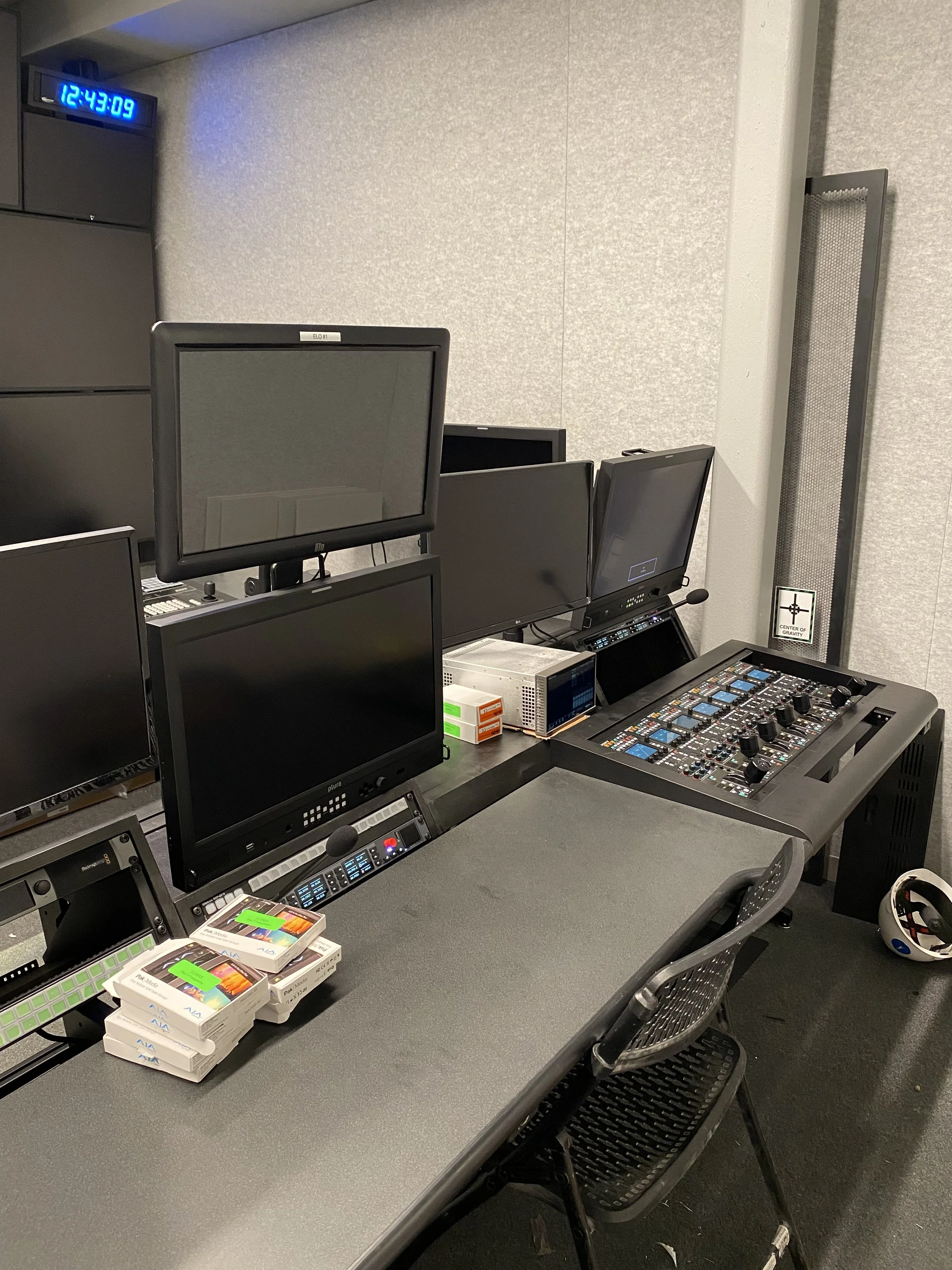 A control room with multiple monitors, computer equipment, and supplies, including a digital clock displaying 12:43:09 in the top left corner.