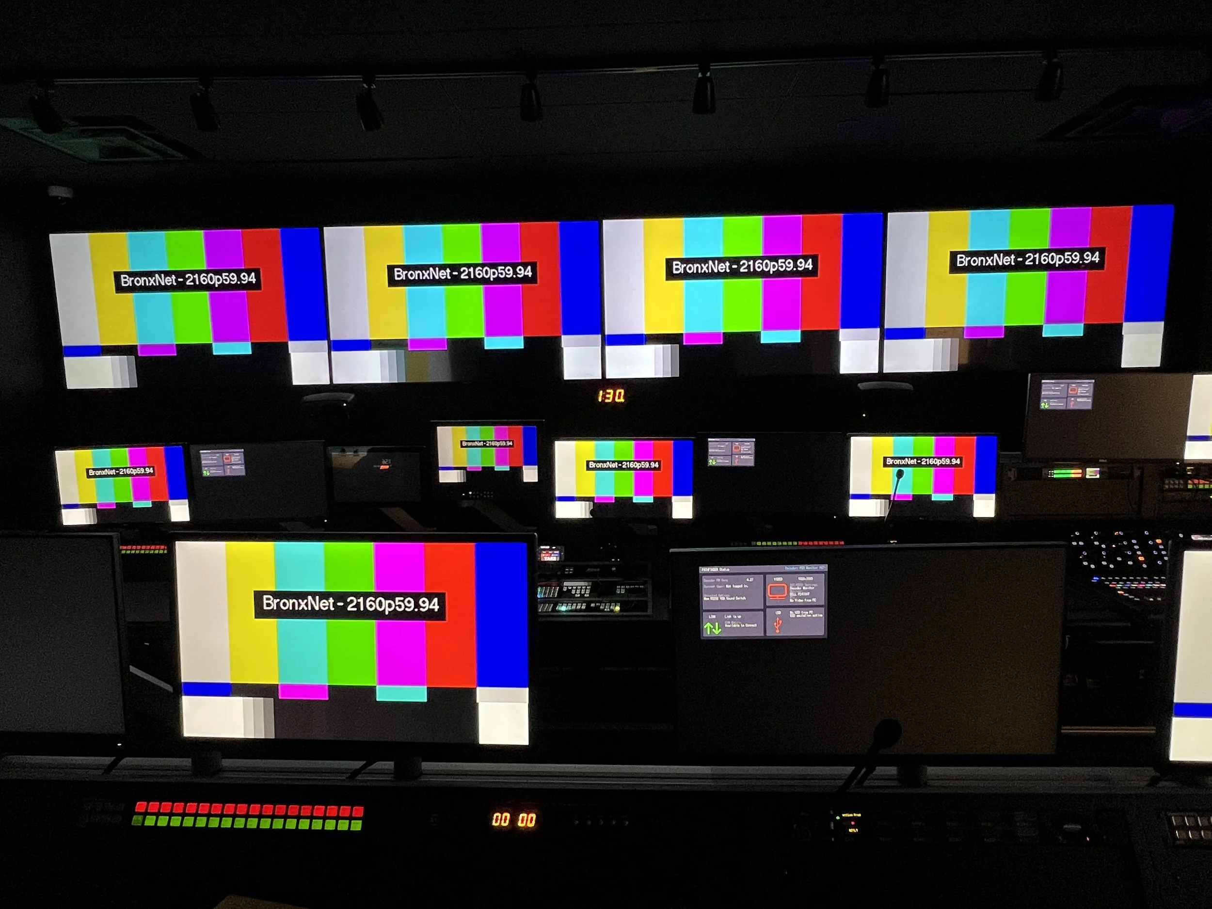 Multiple computer screens displaying color test patterns with vertical color bars and the text 'BronxNet - 2160p59.94'. The room appears to be a control room for video or broadcasting equipment.