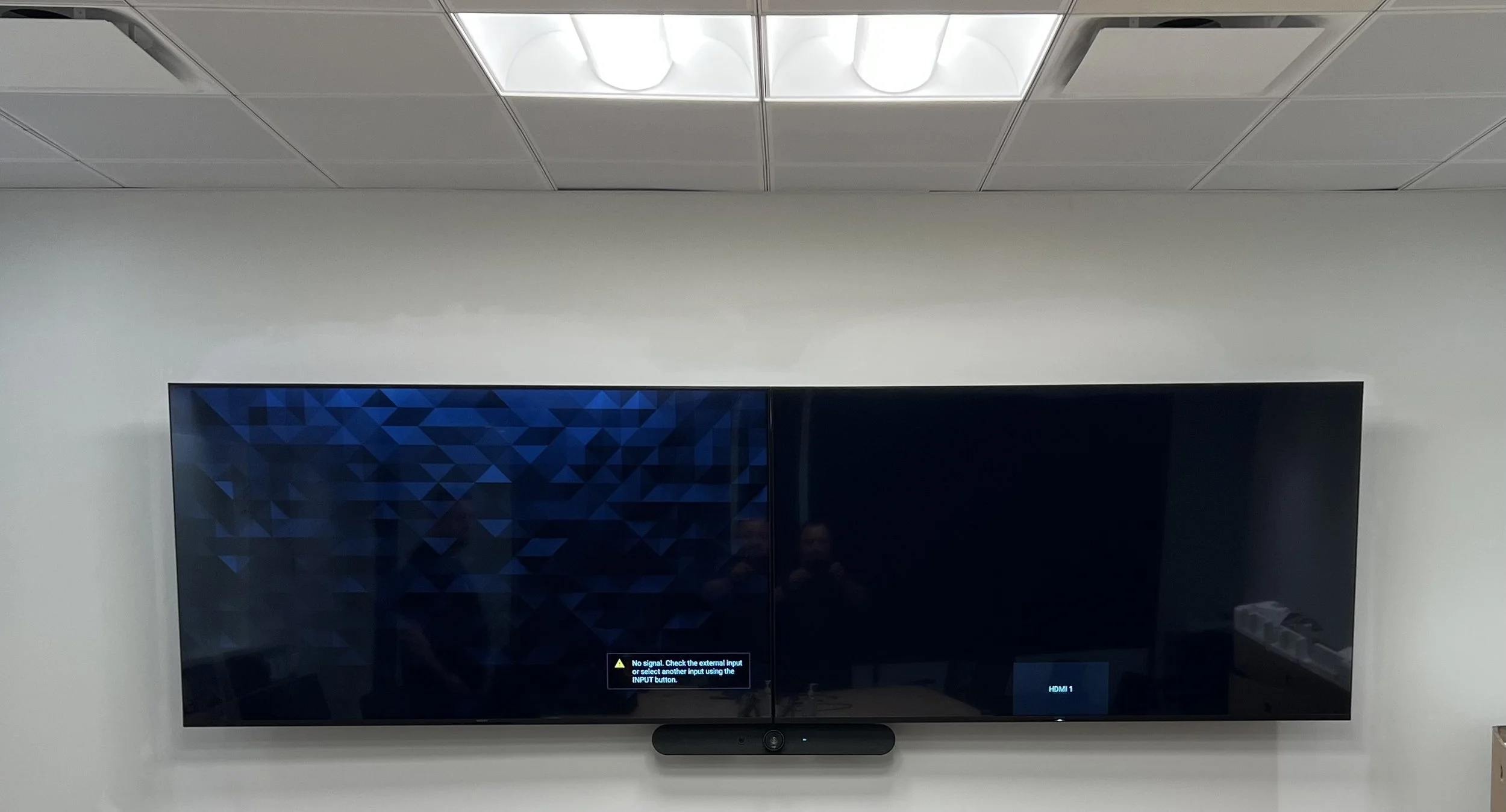 A flat-screen television mounted on a white wall showing an error message with a blue geometric background and a black screen to the right.